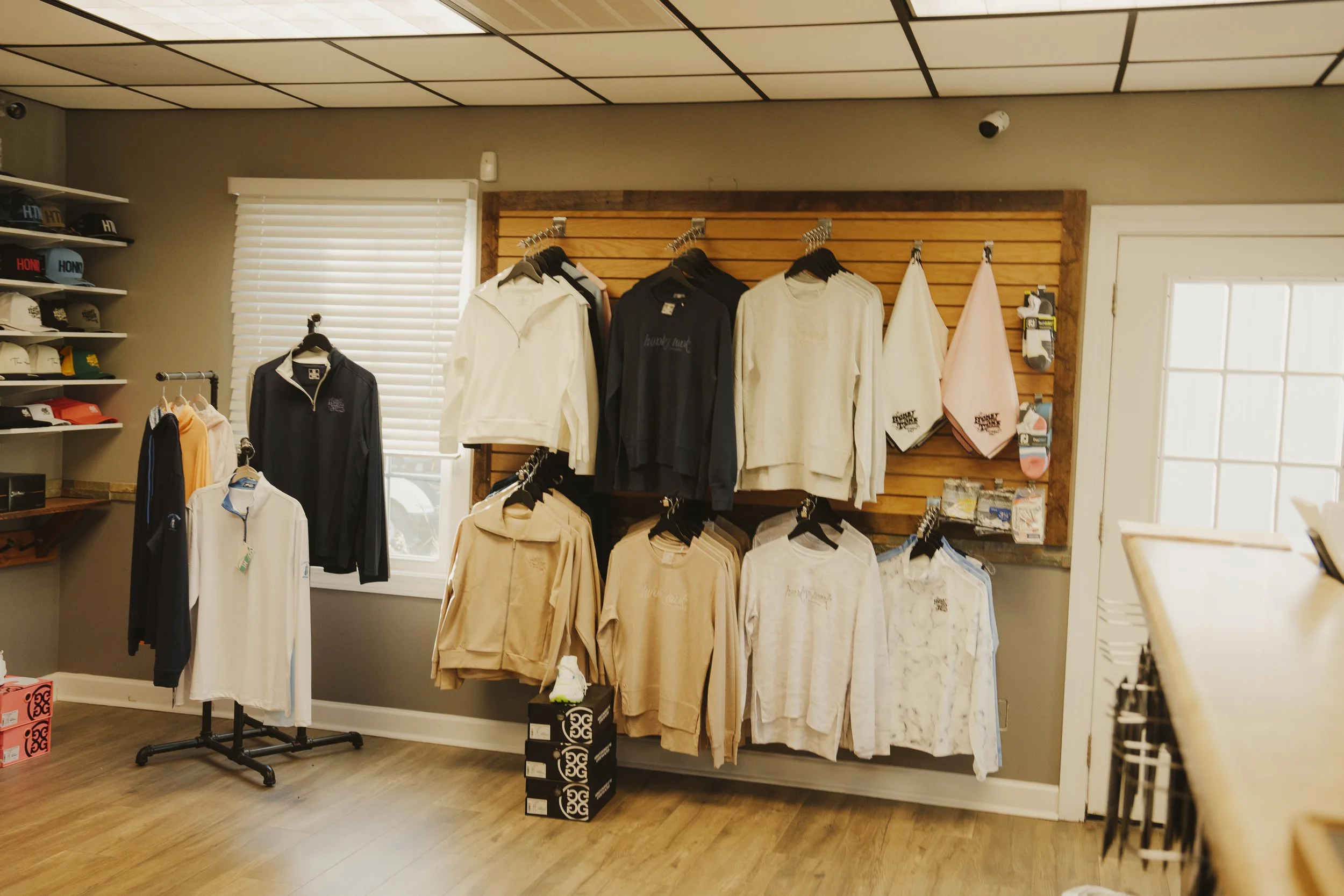 Clothing store display with various jackets and sweatshirts on black hangers, hats on shelves, and towels hanging on hooks.