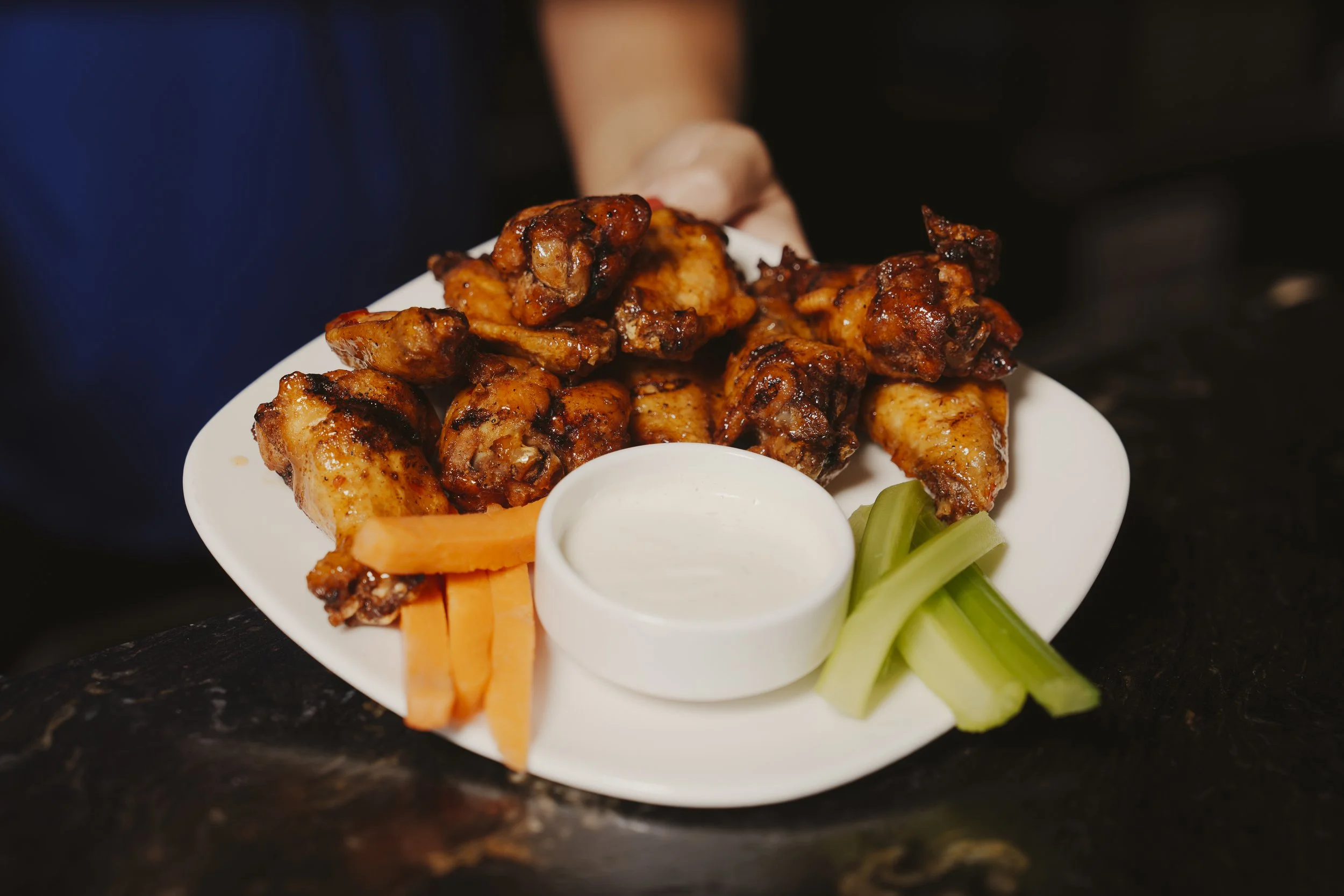 Plate of grilled chicken wings with celery sticks, carrot sticks, and a side of ranch dipping sauce.