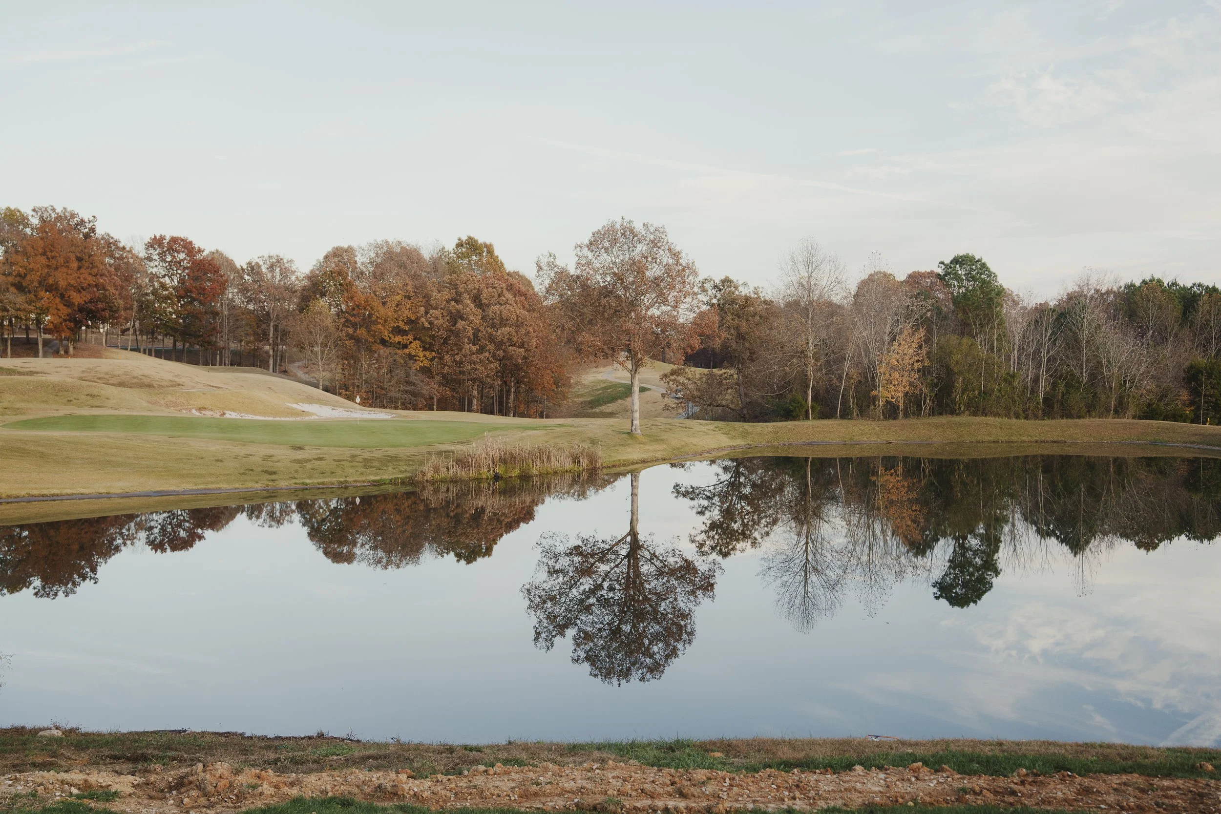 A calm golf course pond reflecting the surrounding trees with autumn foliage on a clear day