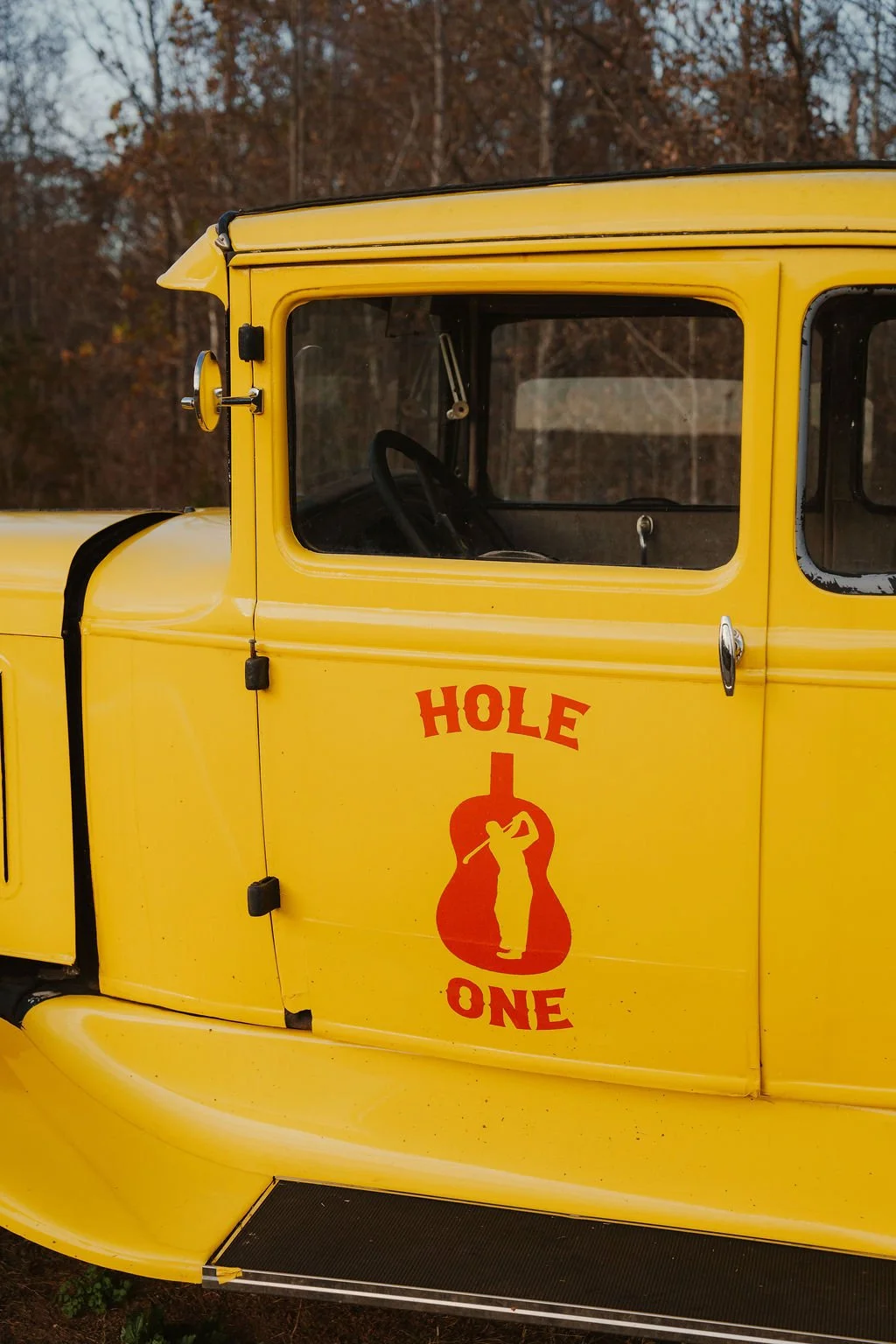 Close-up of a yellow vintage truck with a sign reading "Hole in One" and a graphic of a golfer in a red circle on the door.