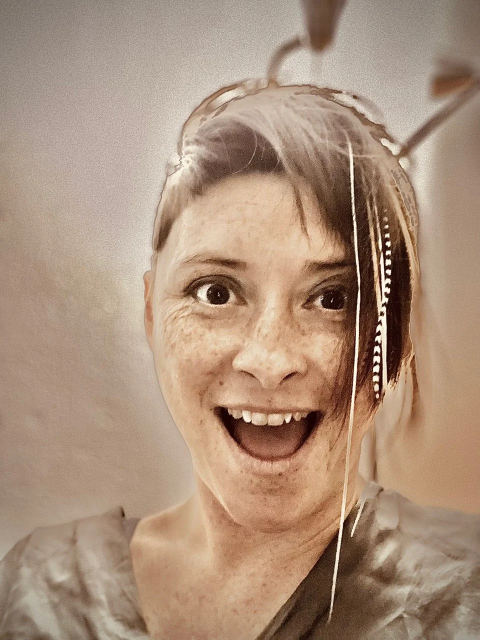 Junge Frau mit kurzen Haaren, lächelnd, mit Feder- und Schmuckdetails im Haar, beim Sticken oder Handarbeiten, die Kamera nach oben gerichtet.