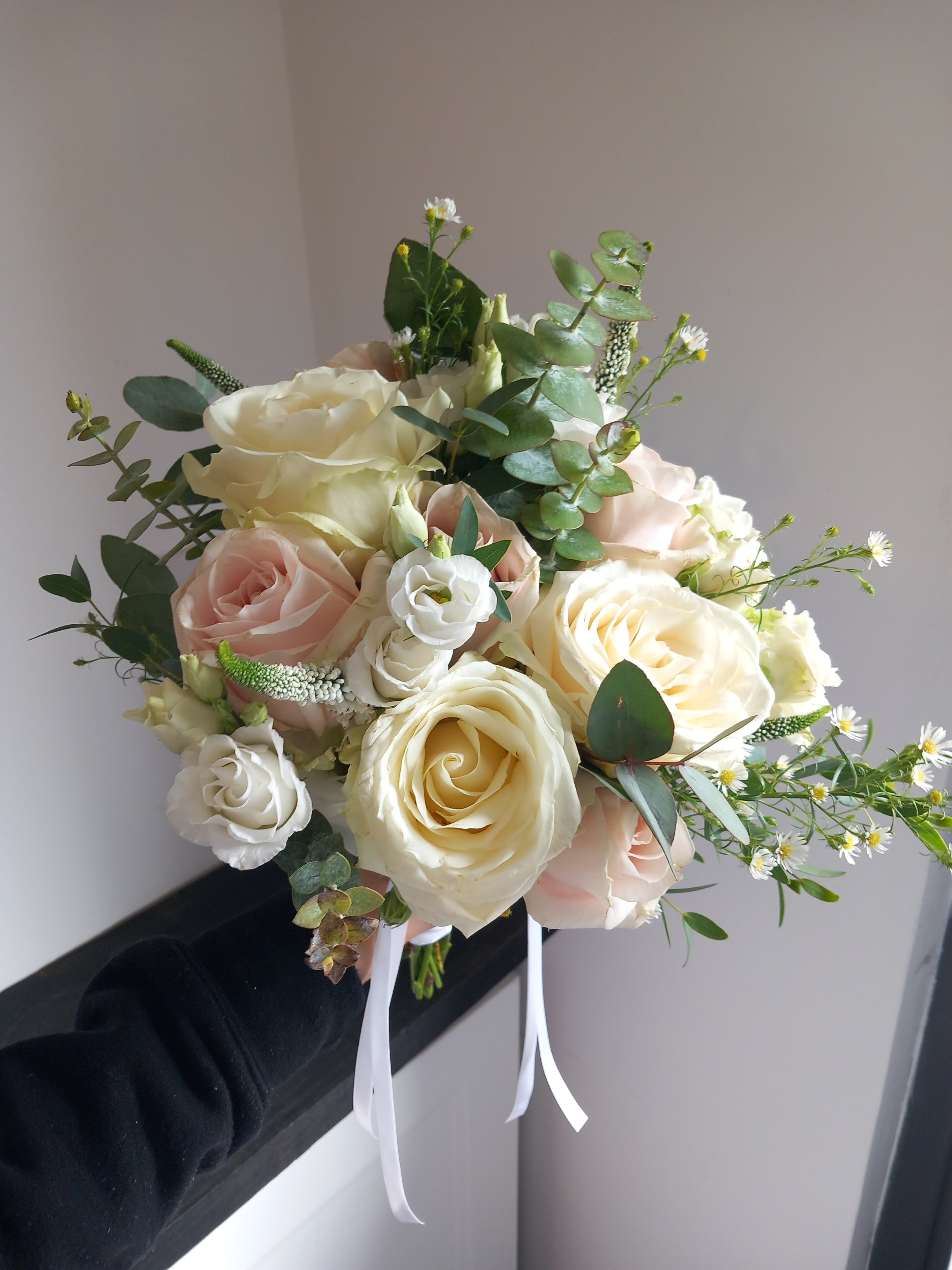 A bridal bouquet with white and pale pink roses, eucalyptus leaves, and small white flowers.