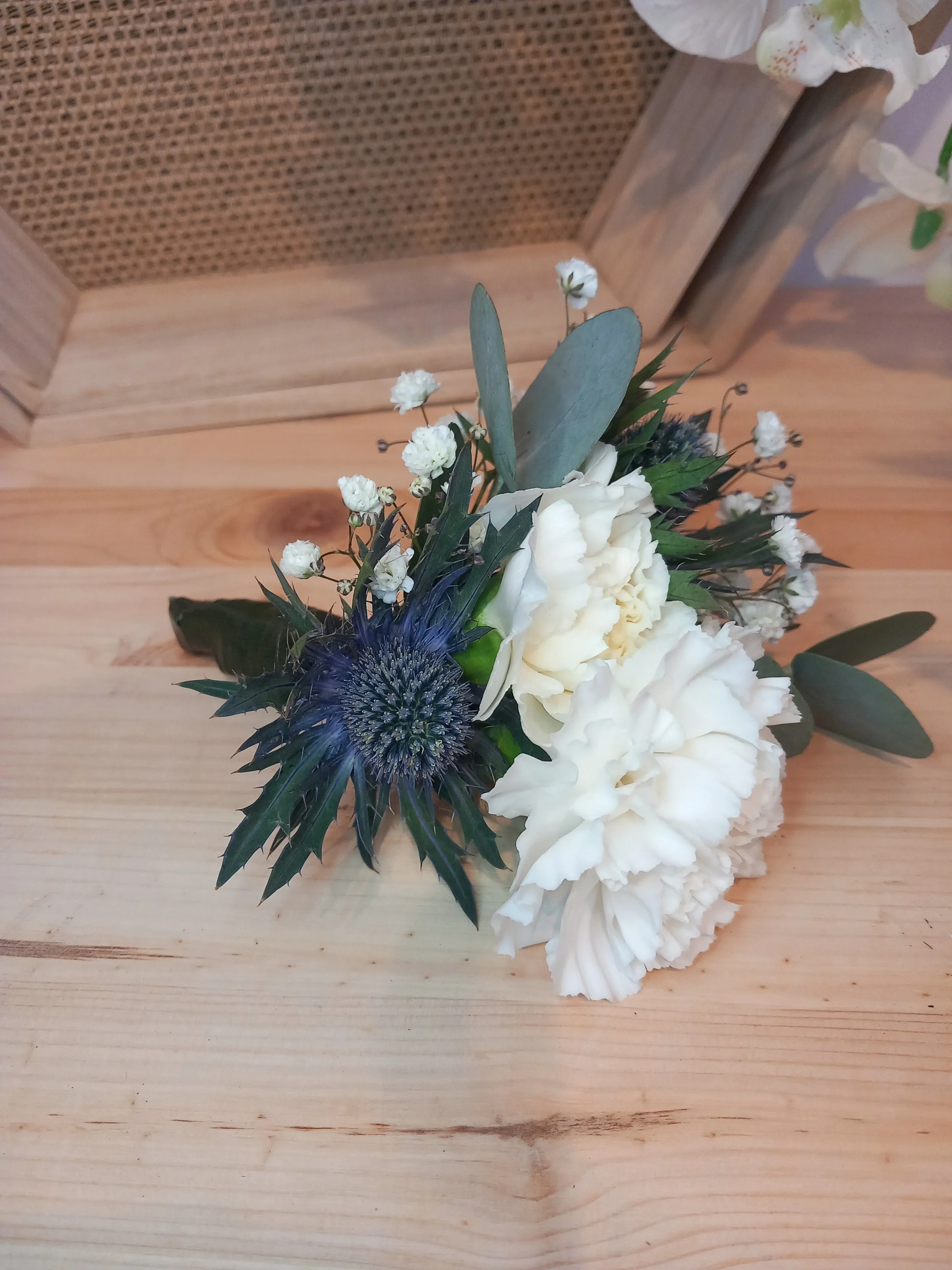 Floral buttonhole with white carnations, blue thistle, and eucalyptus for a wedding or prom.