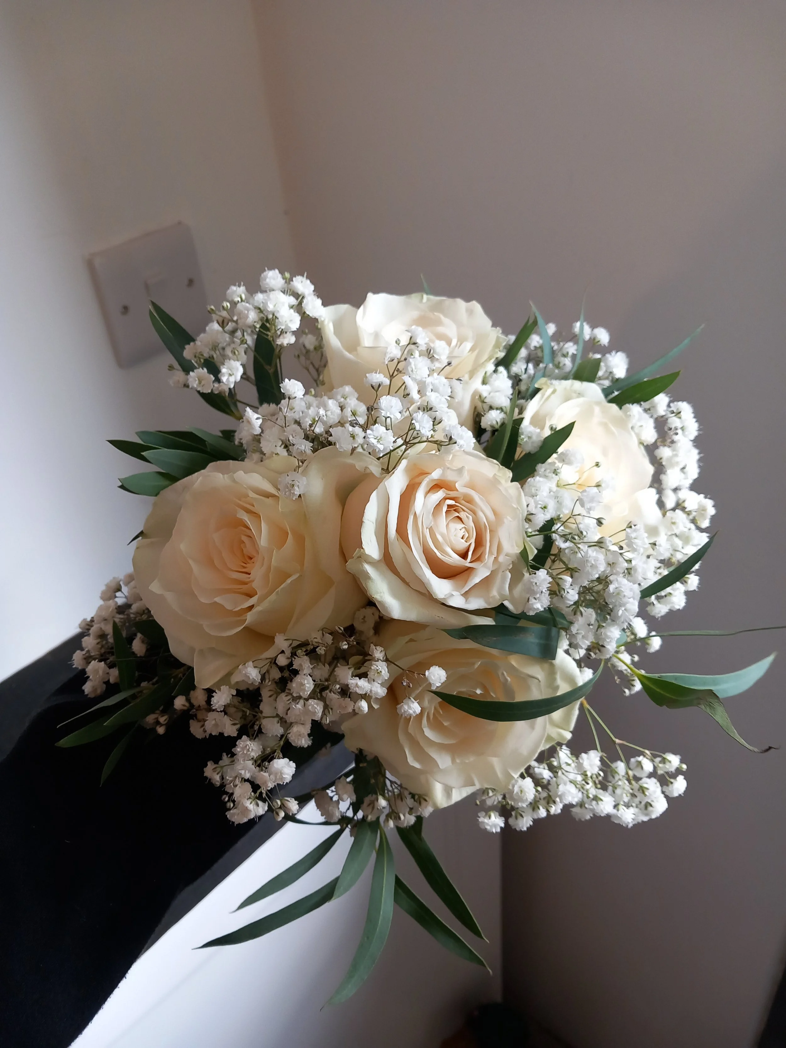 A bouquet of white roses, baby's breath, and green leaves.