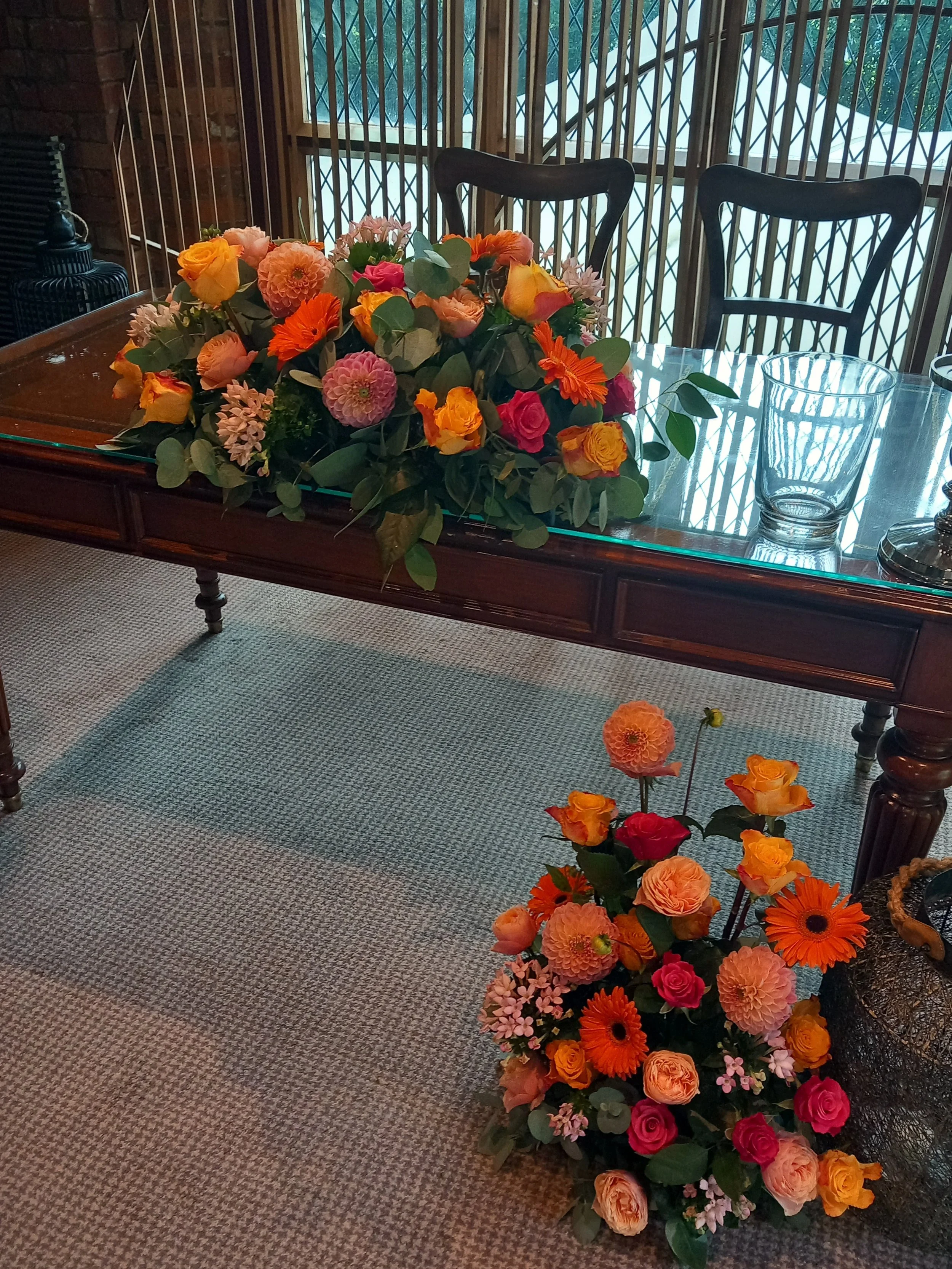 A large wedding reception table arrangement of colourful flowers on a wooden dining table, with a smaller matching floral floor arrangement, in the Clandeboye Hotel Belfast