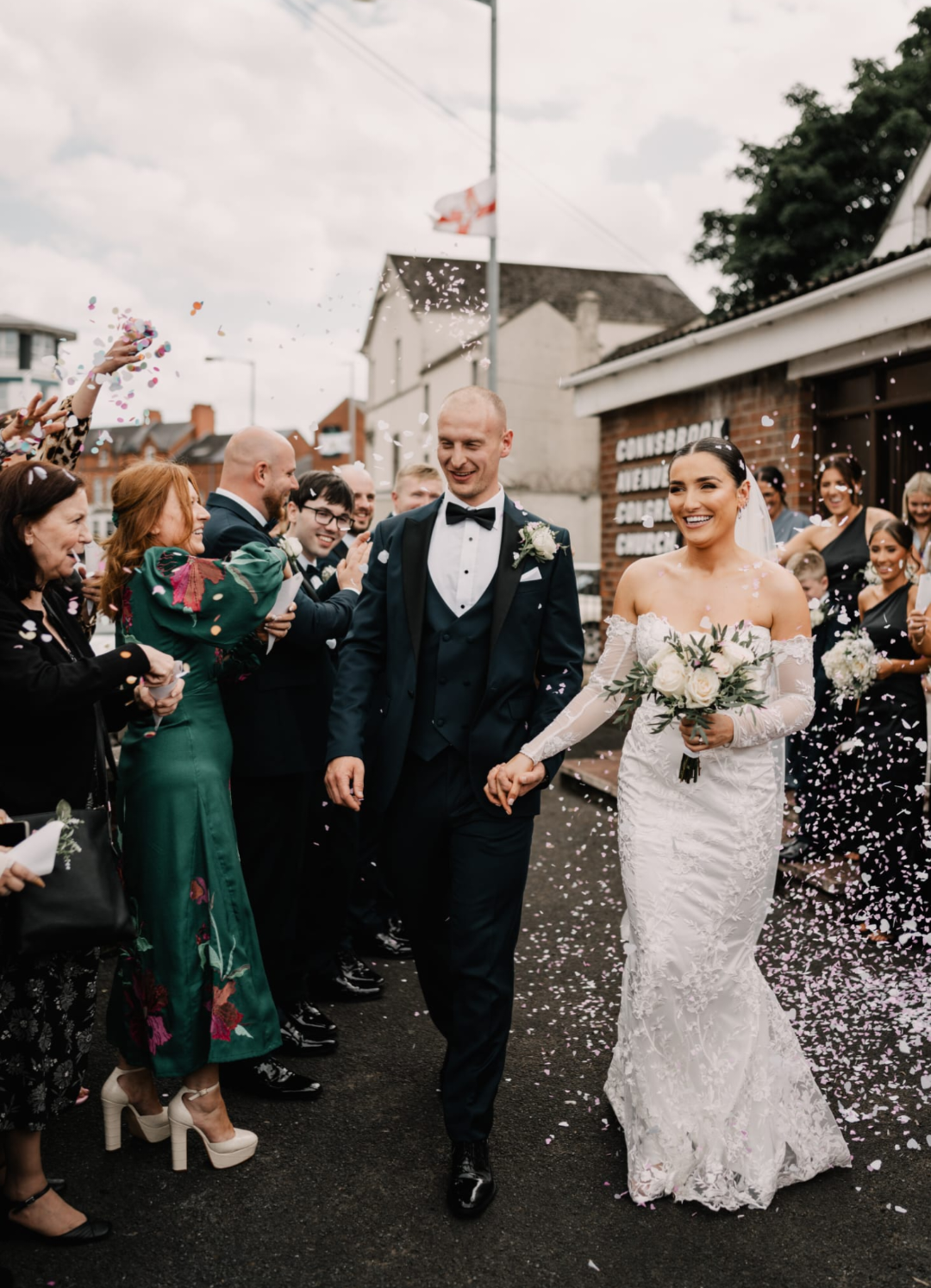 A newlywed couple walking hand-in-hand outside, surrounded by friends and family throwing confetti during the wedding celebration.