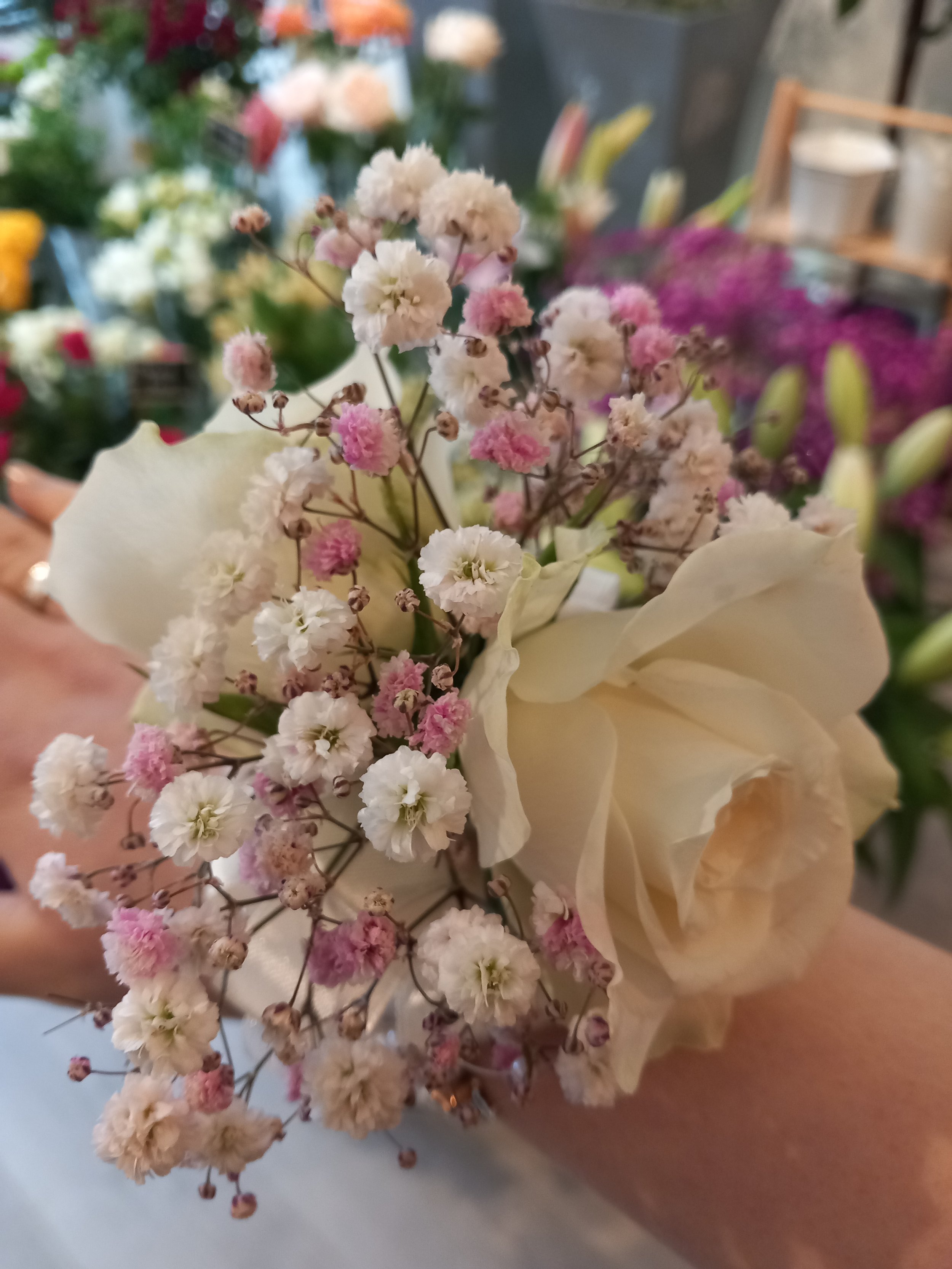 Close-up of a beige rose and pink and white baby's breath wrist corsage for a wedding guest.