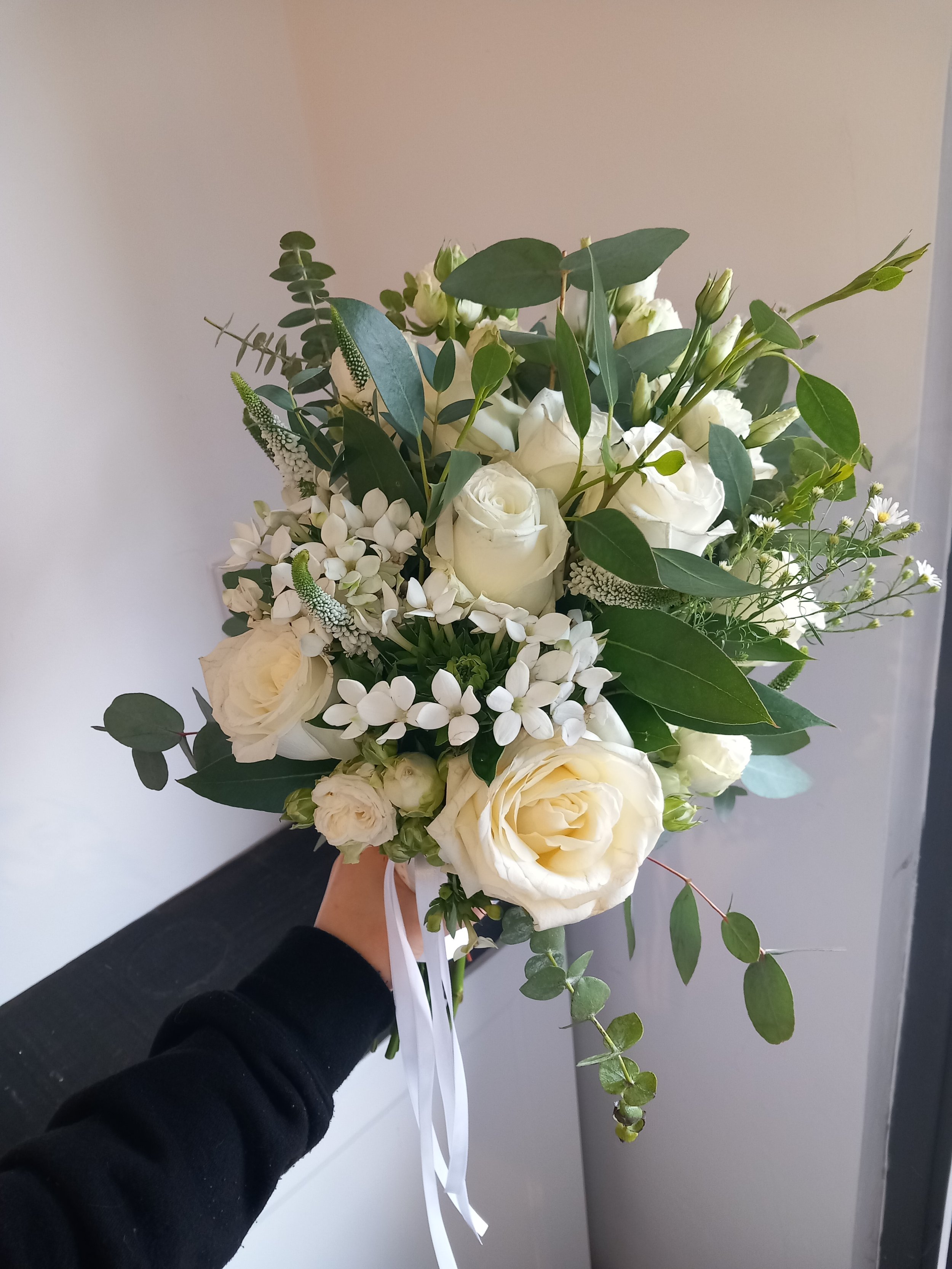 Bridal bouquet with white roses, lisianthus, phlox, veronica, september flower, eucalyptus leaves, and white ribbon