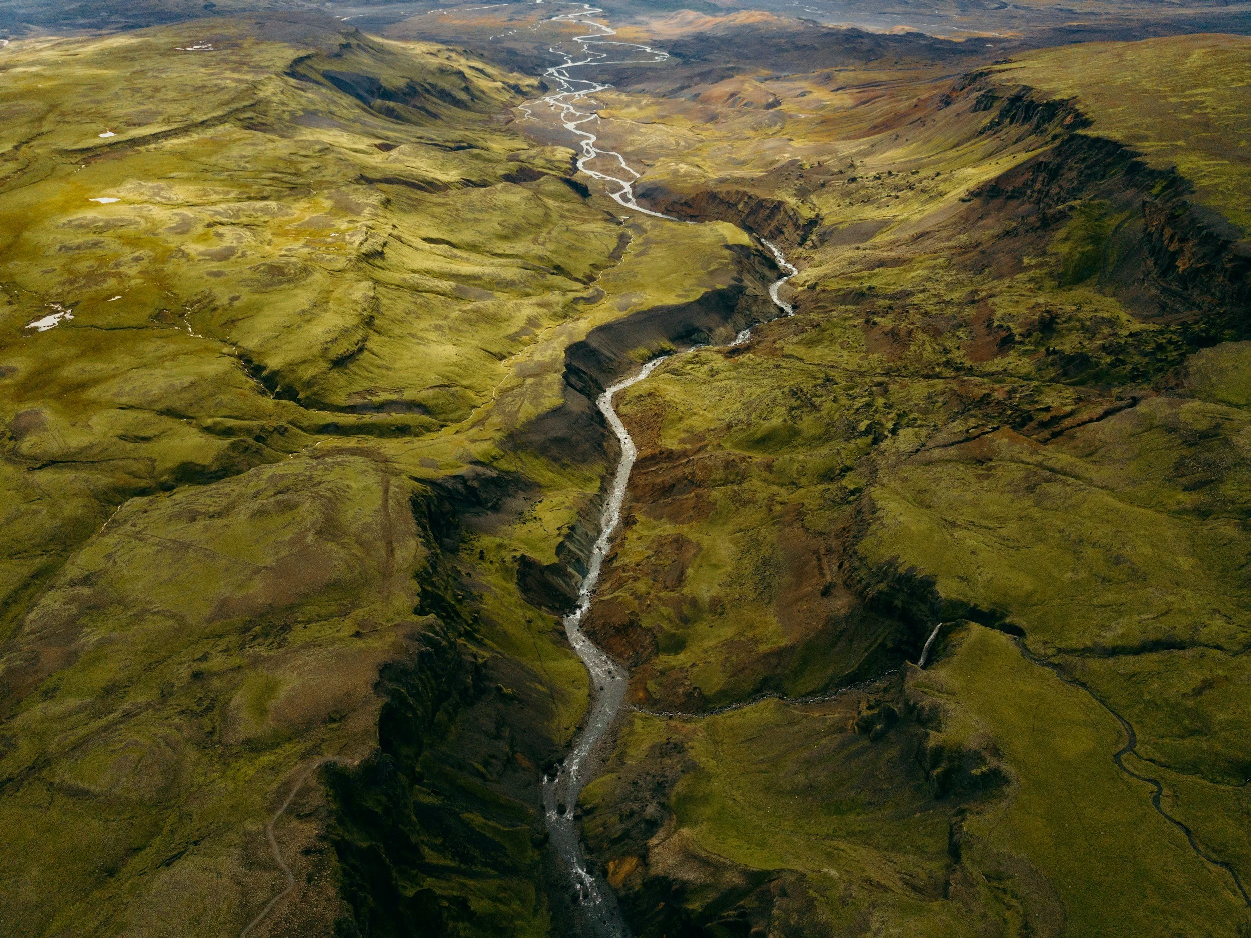 Aerial view of a green canyon with river valleys and waterfalls in a remote landscape.
