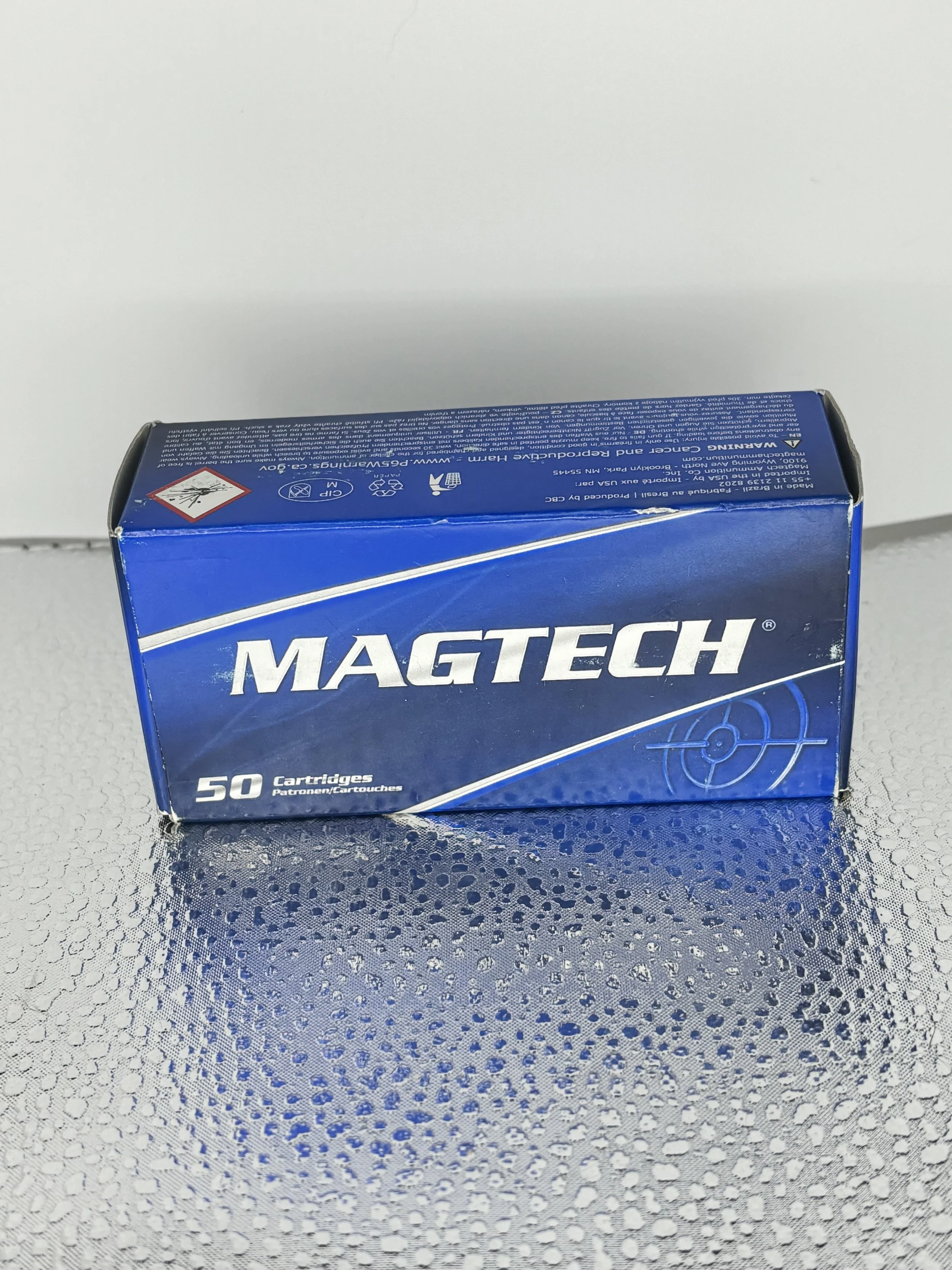 Blue box of Magtech ammunition with 50 cartridges on a textured metallic surface.