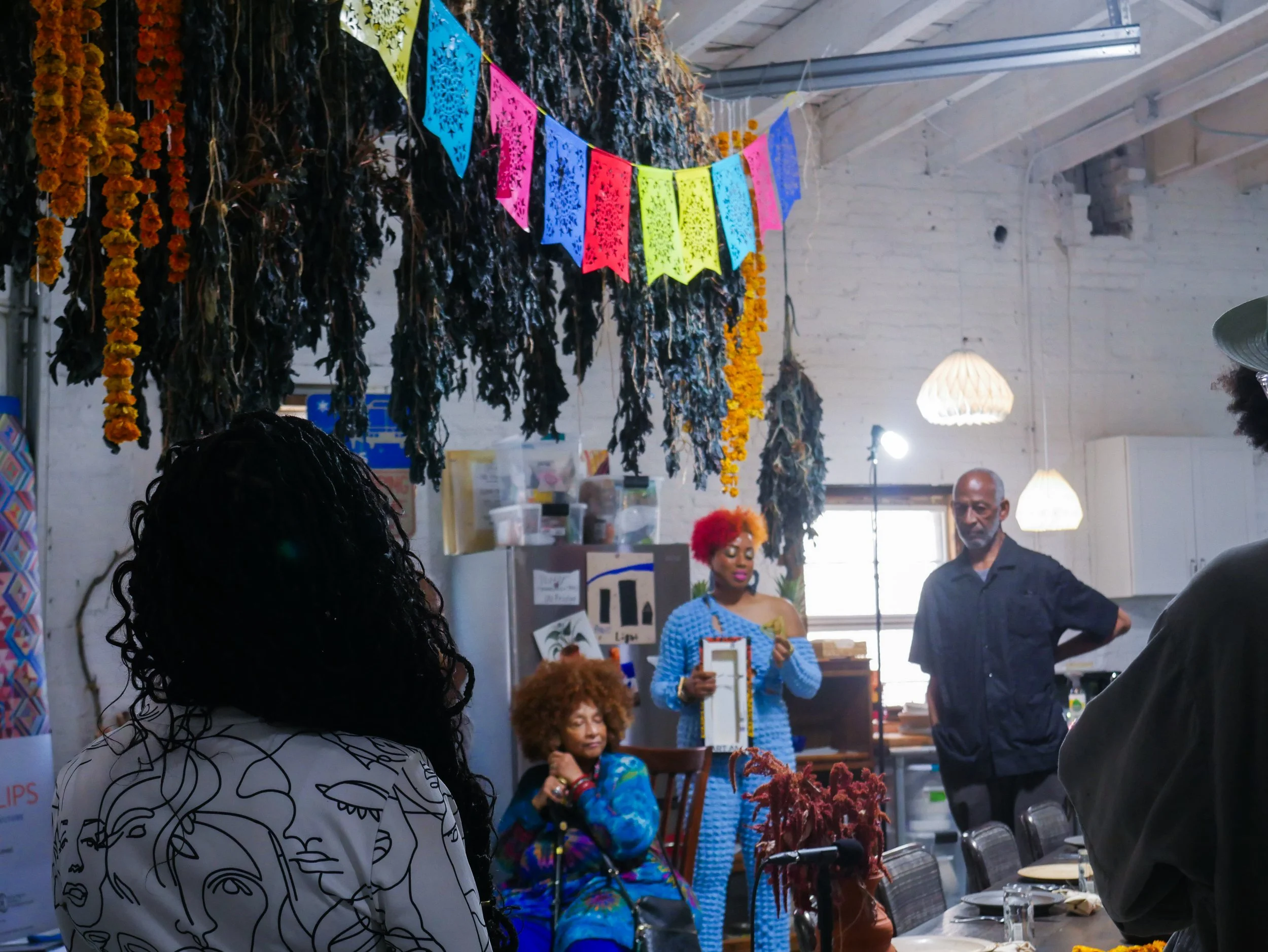 Community members arrive for a Mixing Bowl gathering in a space decorated with marigold garlands.