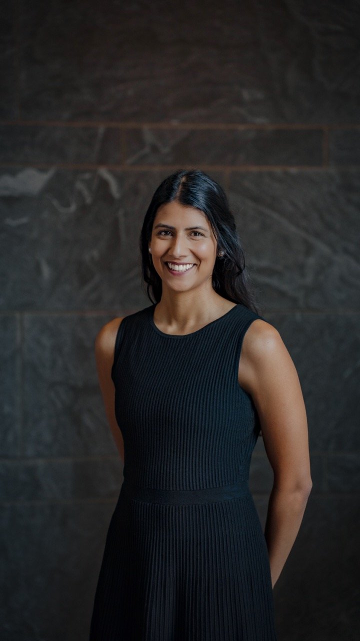 Photograph of FSC founder Niyeti Shah – woman with long dark hair is smiling and wearing a sleeveless black dress, standing against a dark marble wall.