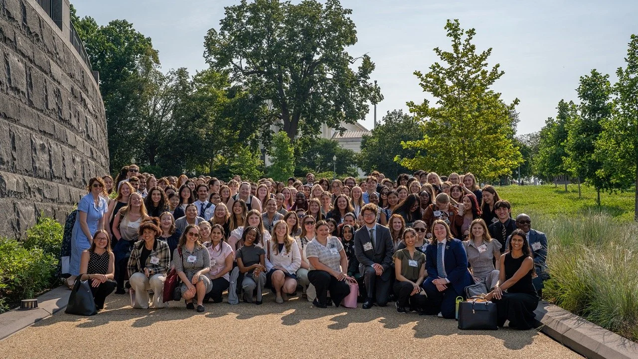 Large group of diverse participants of the 2026 Gen Z Food and Hunger Summit posing outdoors for a photo on a sunny day, with trees and a stone wall in the background.