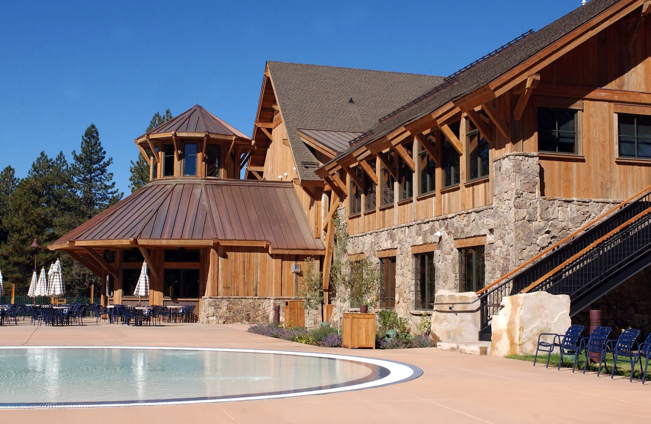 Rustic lodge building with stone and wood accents, outdoor seating area with tables and umbrellas, and a small reflecting pool.