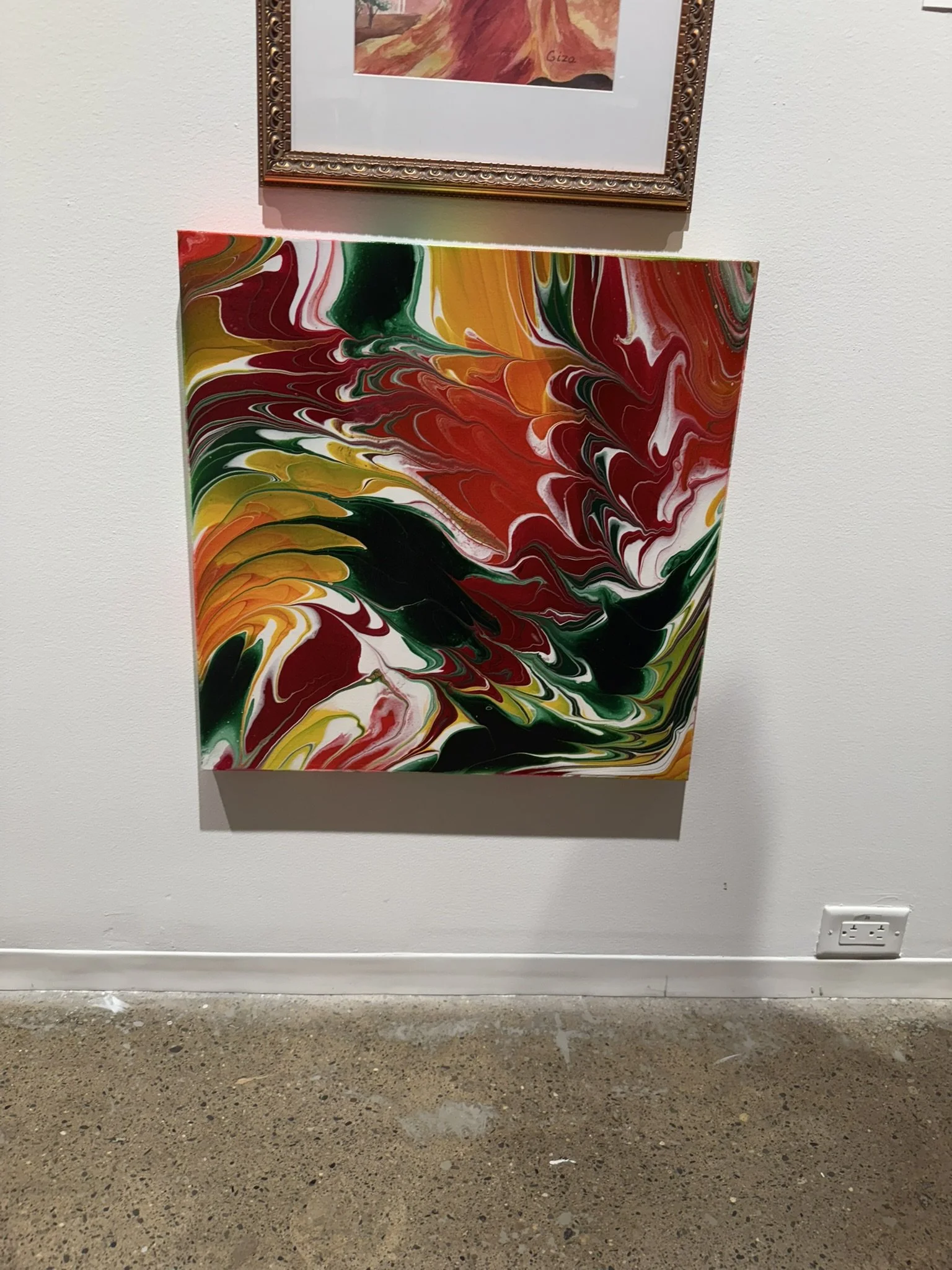 An abstract swirl painting with red, green, yellow, white, and black colors, hung on a white wall.