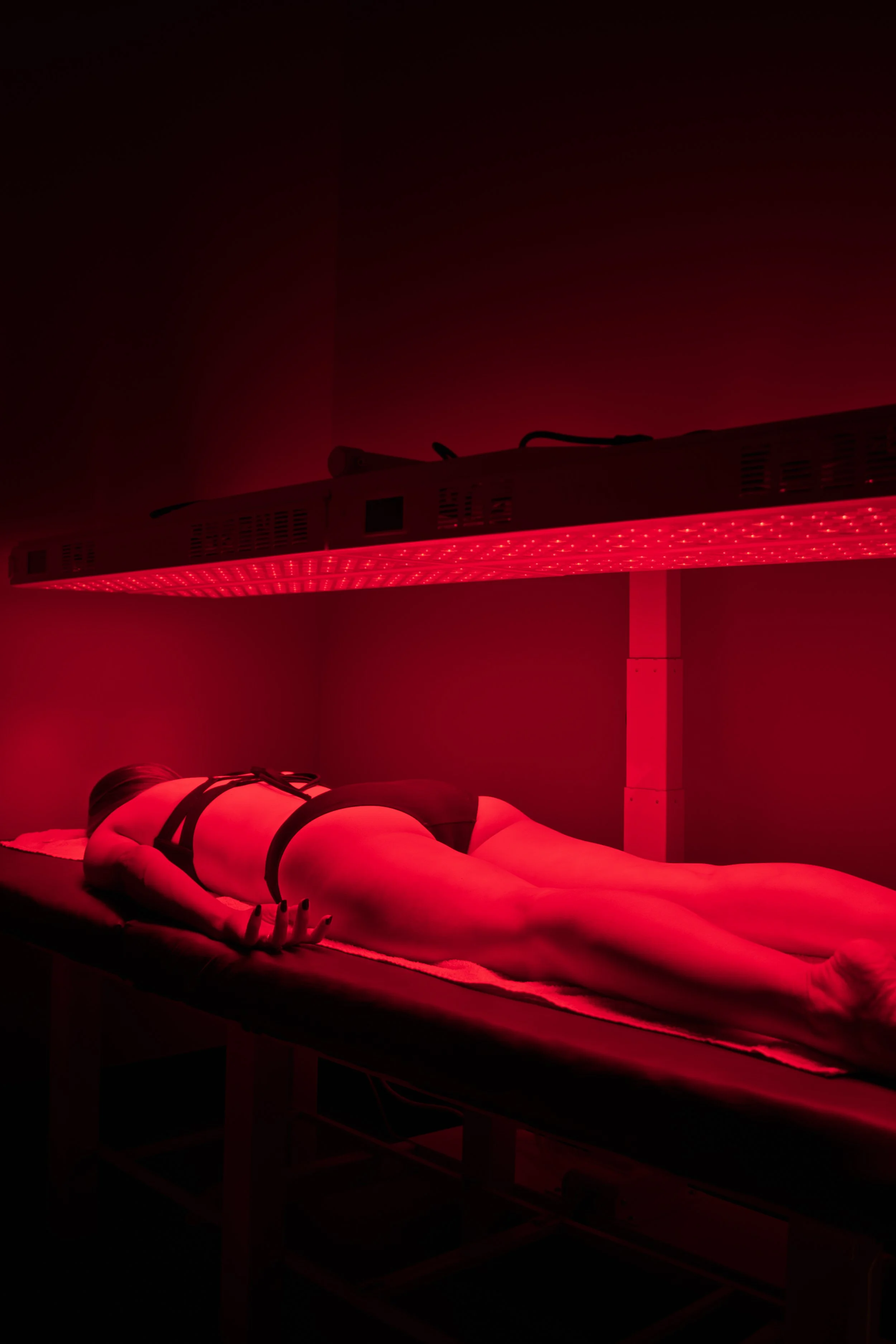 Person lying face down on a massage table under red LED light therapy, with the therapist not visible.