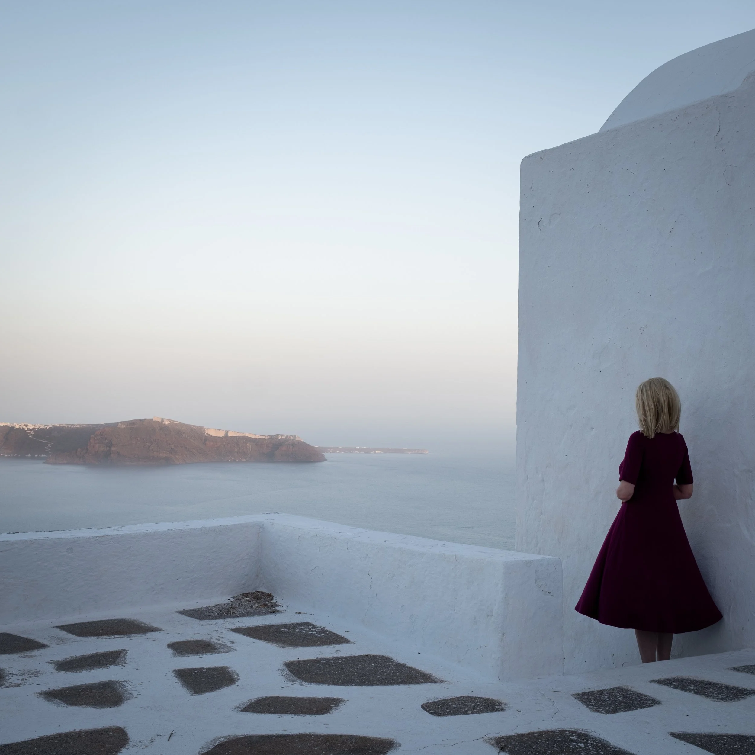 Woman in burgundy dress beside white coastal architecture