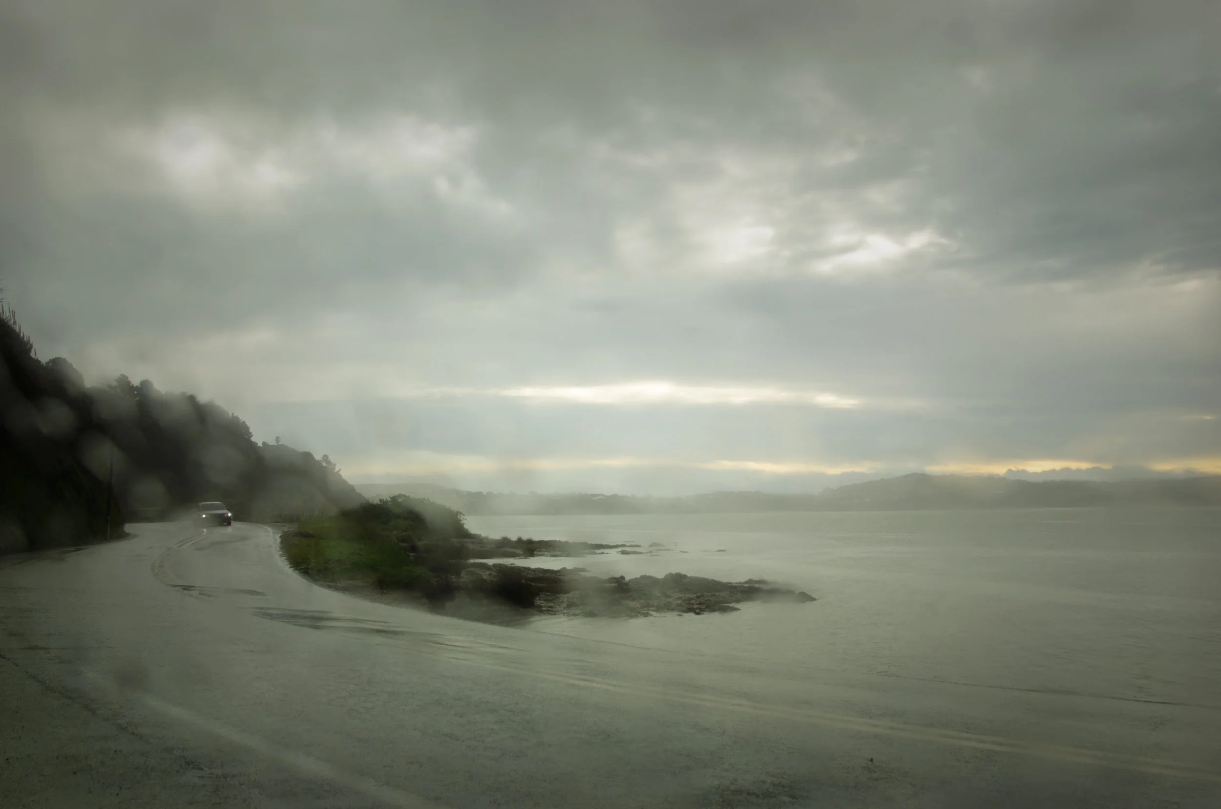 Rainy coastal road seen through car window