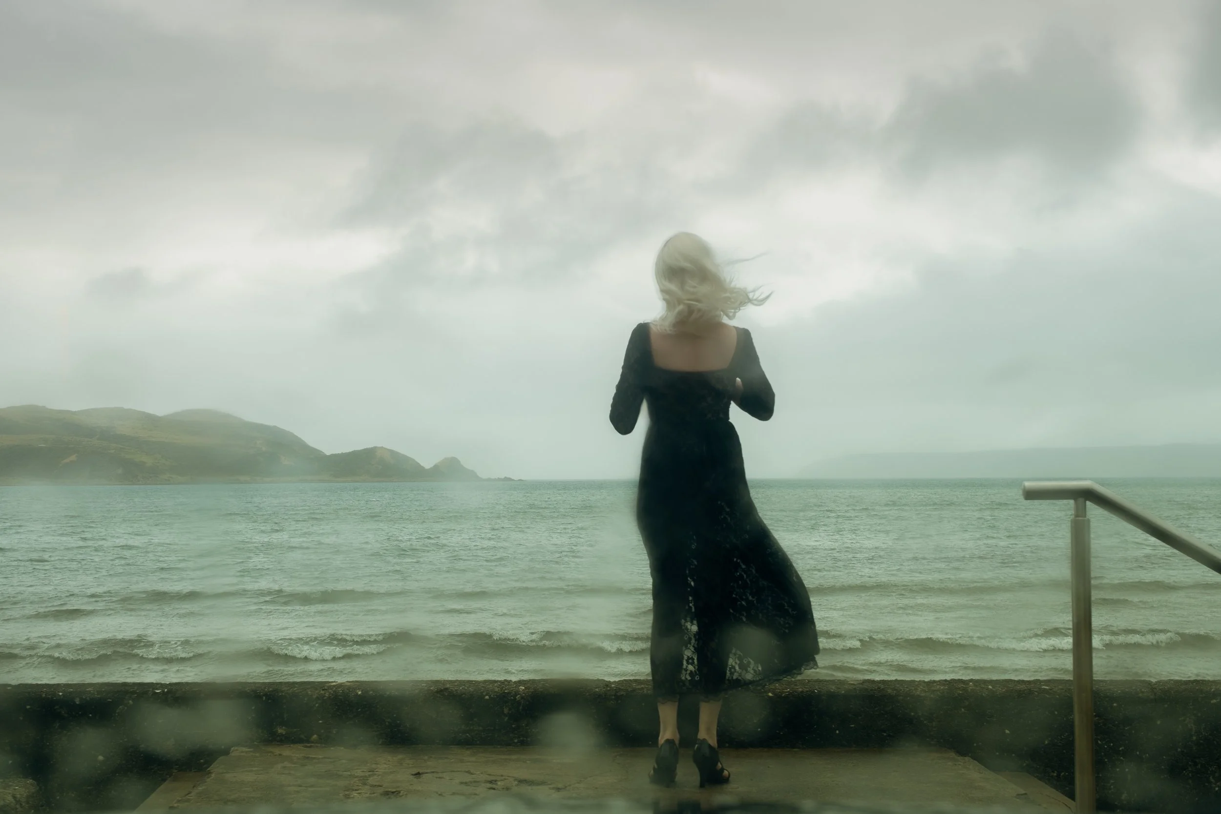 Woman in black dress beside stormy sea