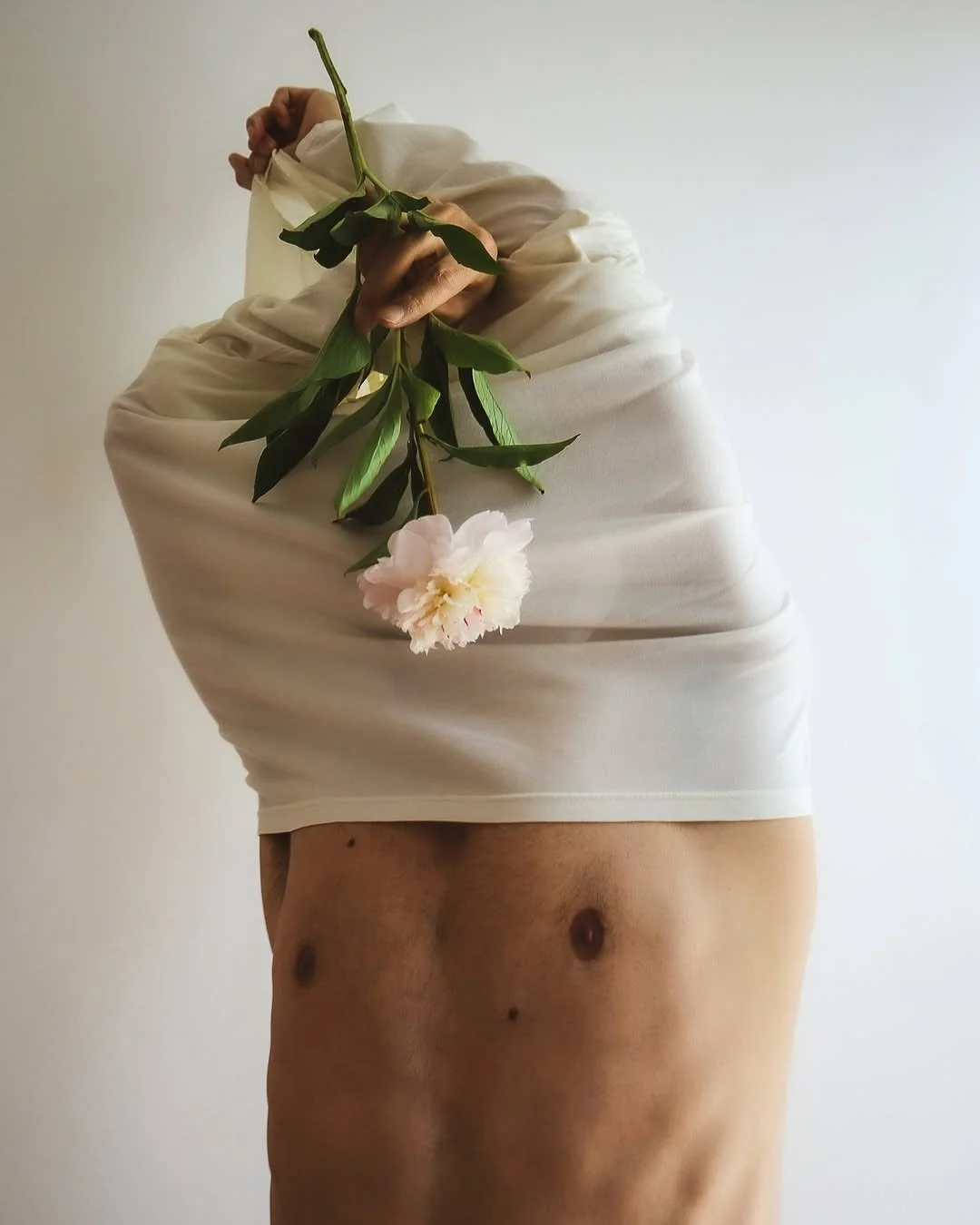 Person lifting their shirt to reveal their abdomen, holding a pink flower and green leaves.
