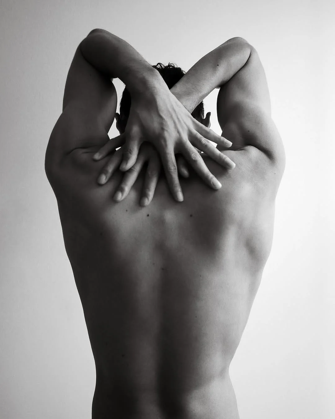 Black and white photograph of a person's back with multiple hands with fingers spread, creating an artistic pattern.