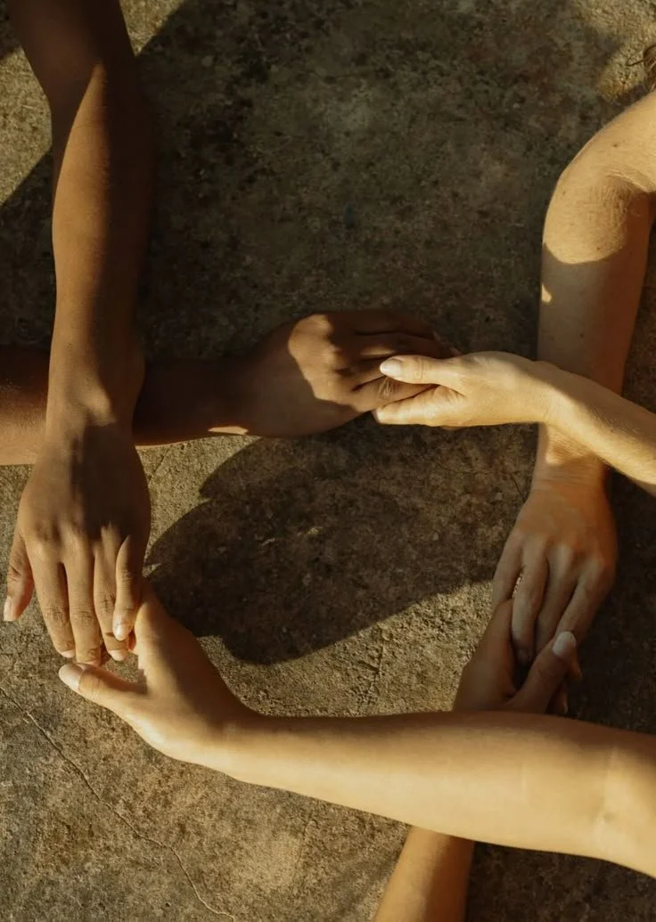 Four hands from different people are connected, forming a square shape on a stone surface.