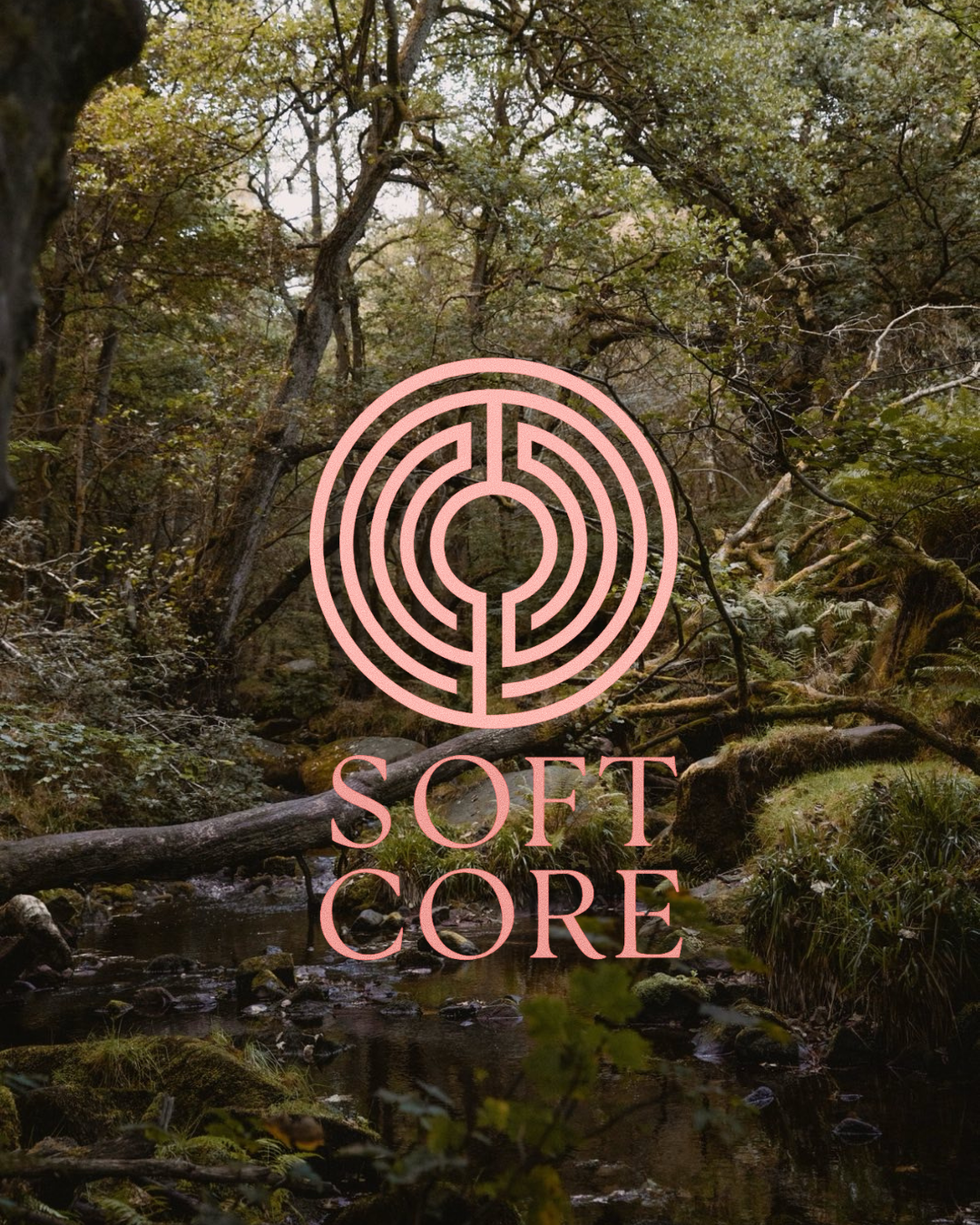 A forest scene with a small stream running through moss-covered rocks and fallen logs. Overlaid is a pink circular maze with the words 'Soft Core' beneath it.