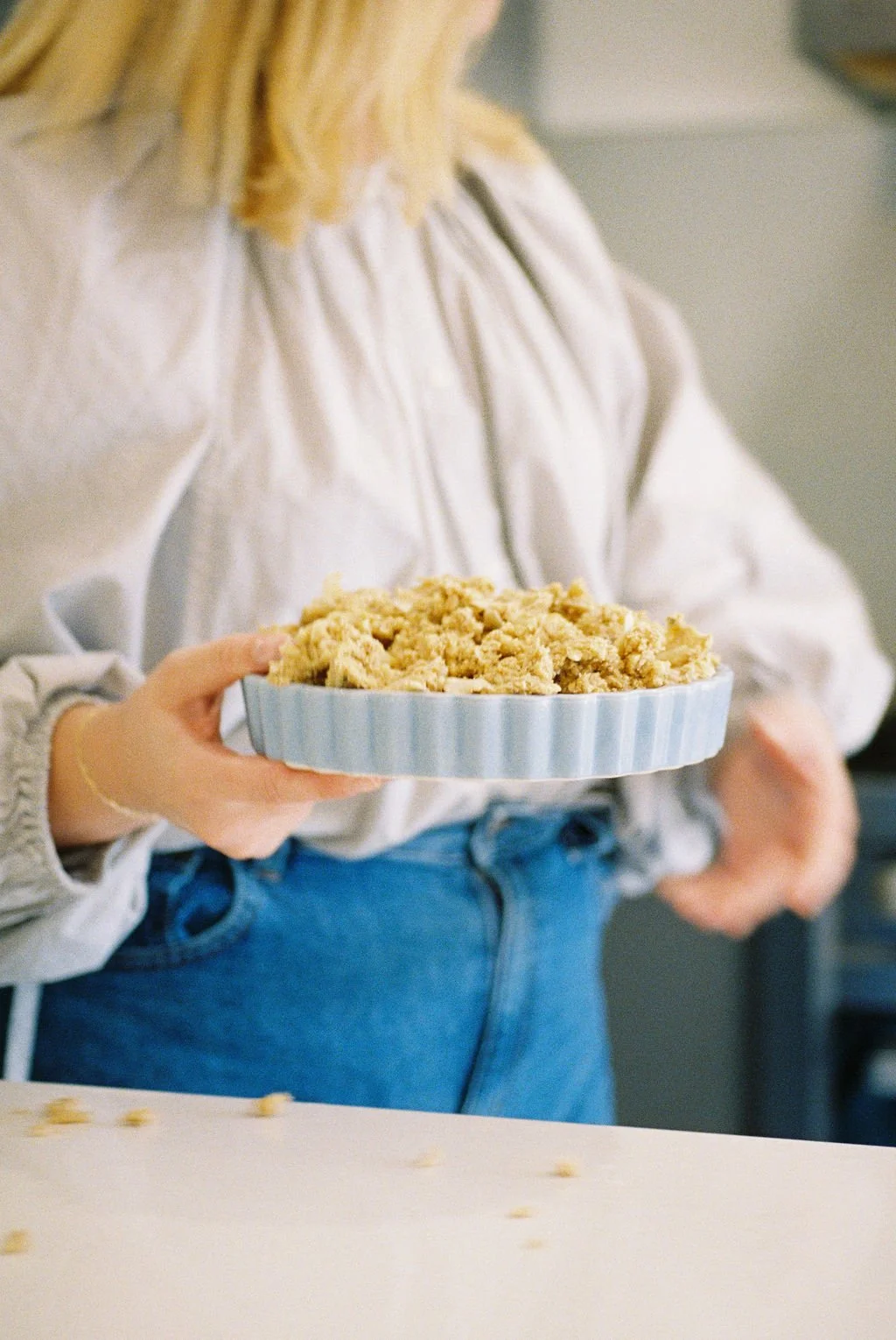 Person holding a pie with crumbles in a photo taken in a kitchen setting.
