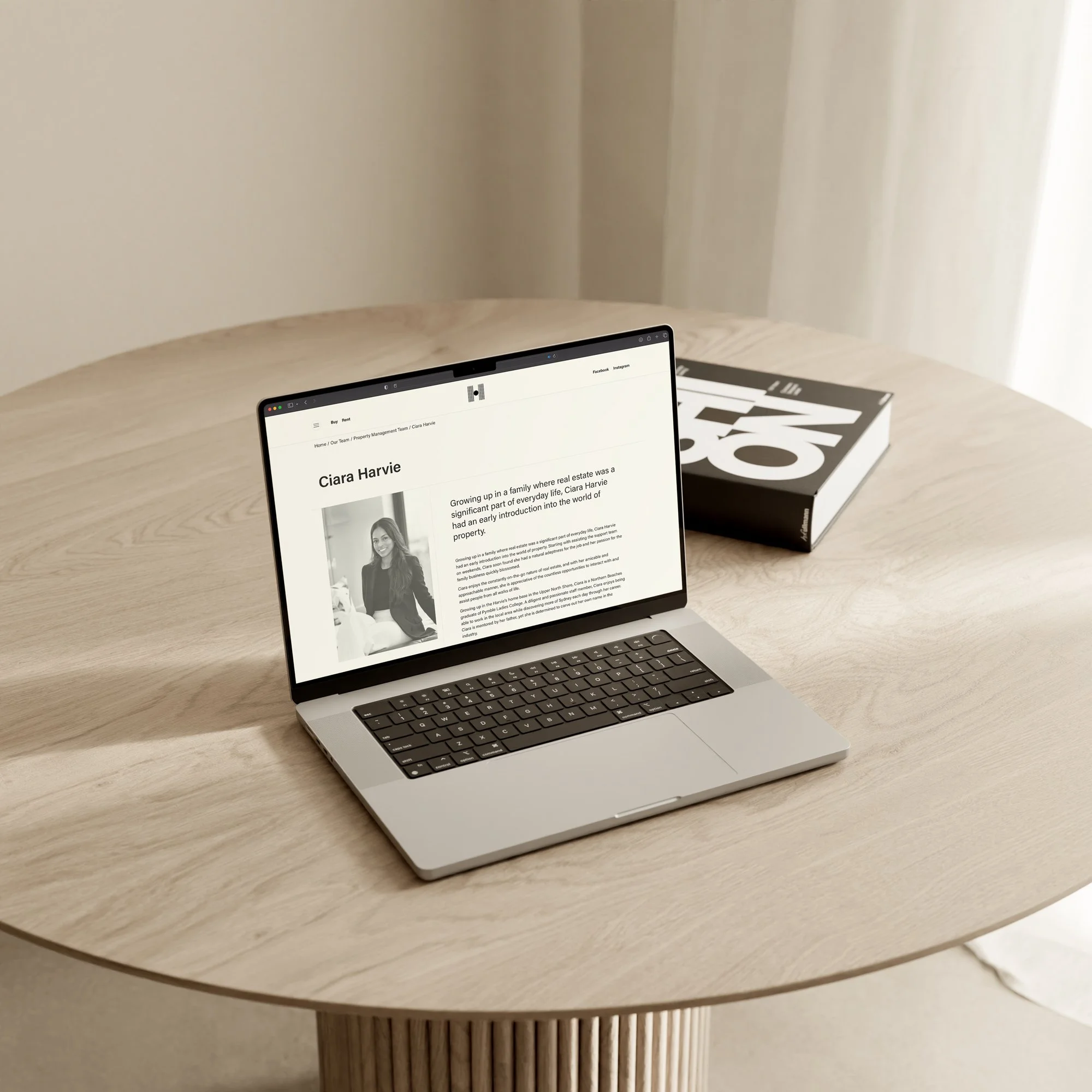 Laptop displaying the Harvie Group website, on a wooden table, with a black and white book beside it.