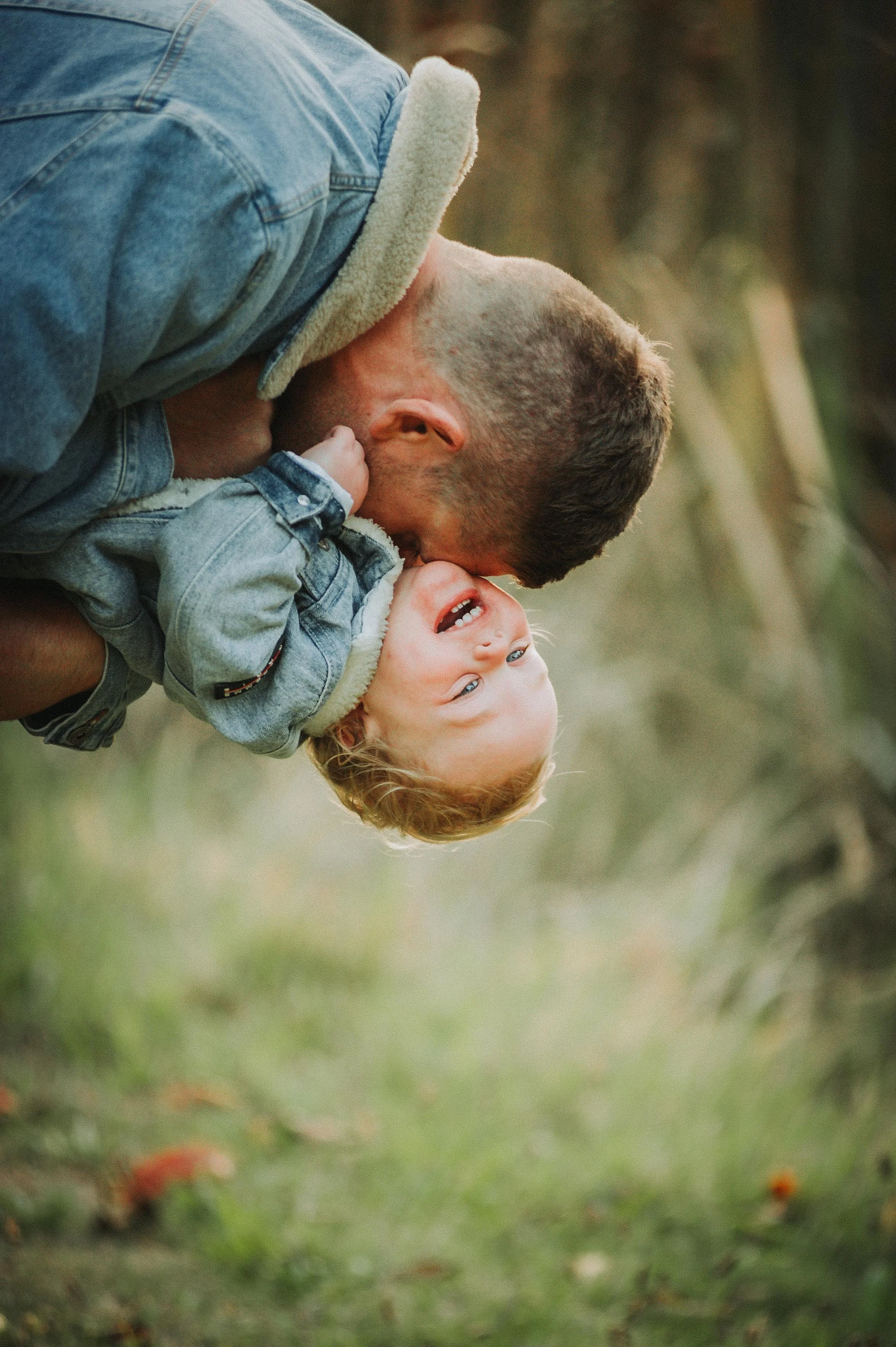 Father playfully holding child upside down outdoors