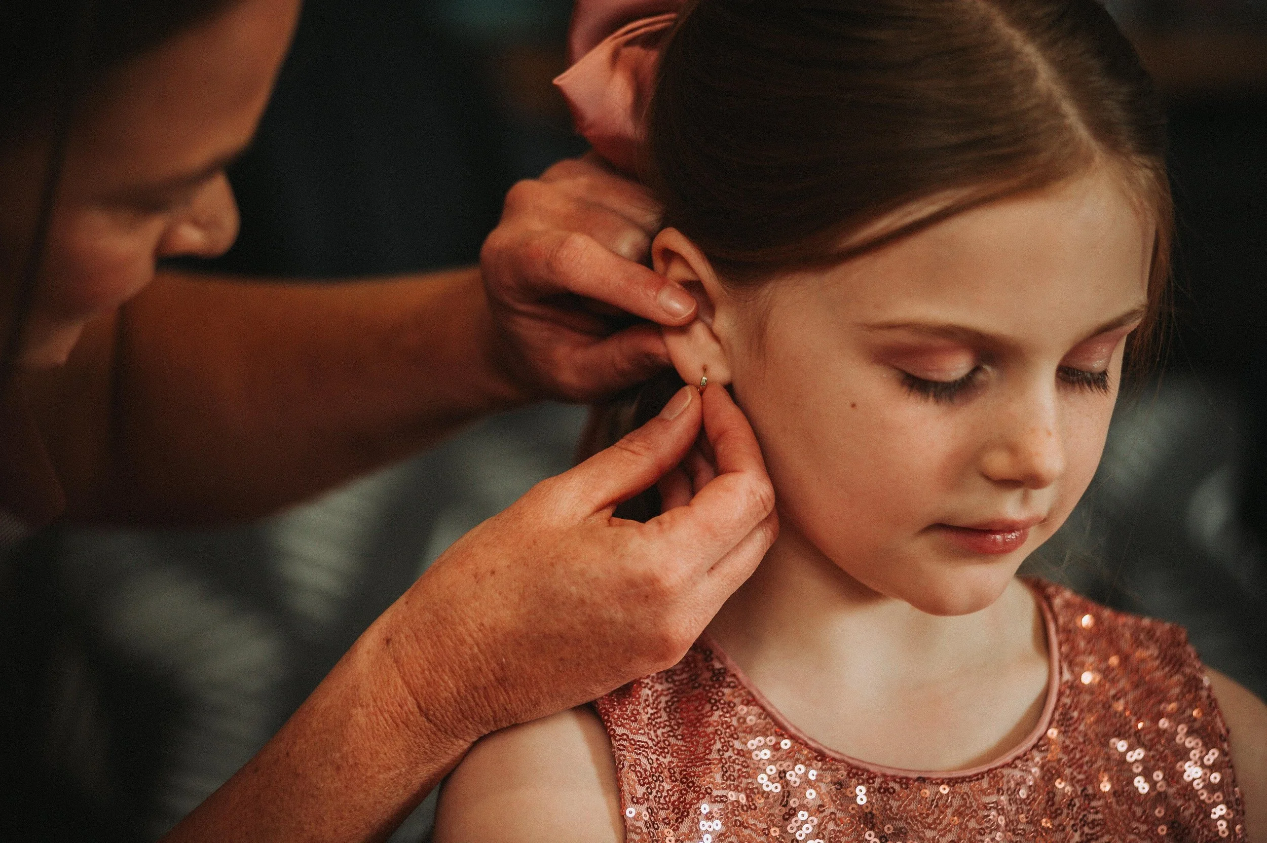Adult helping child put on an earring, child wearing a sequined dress