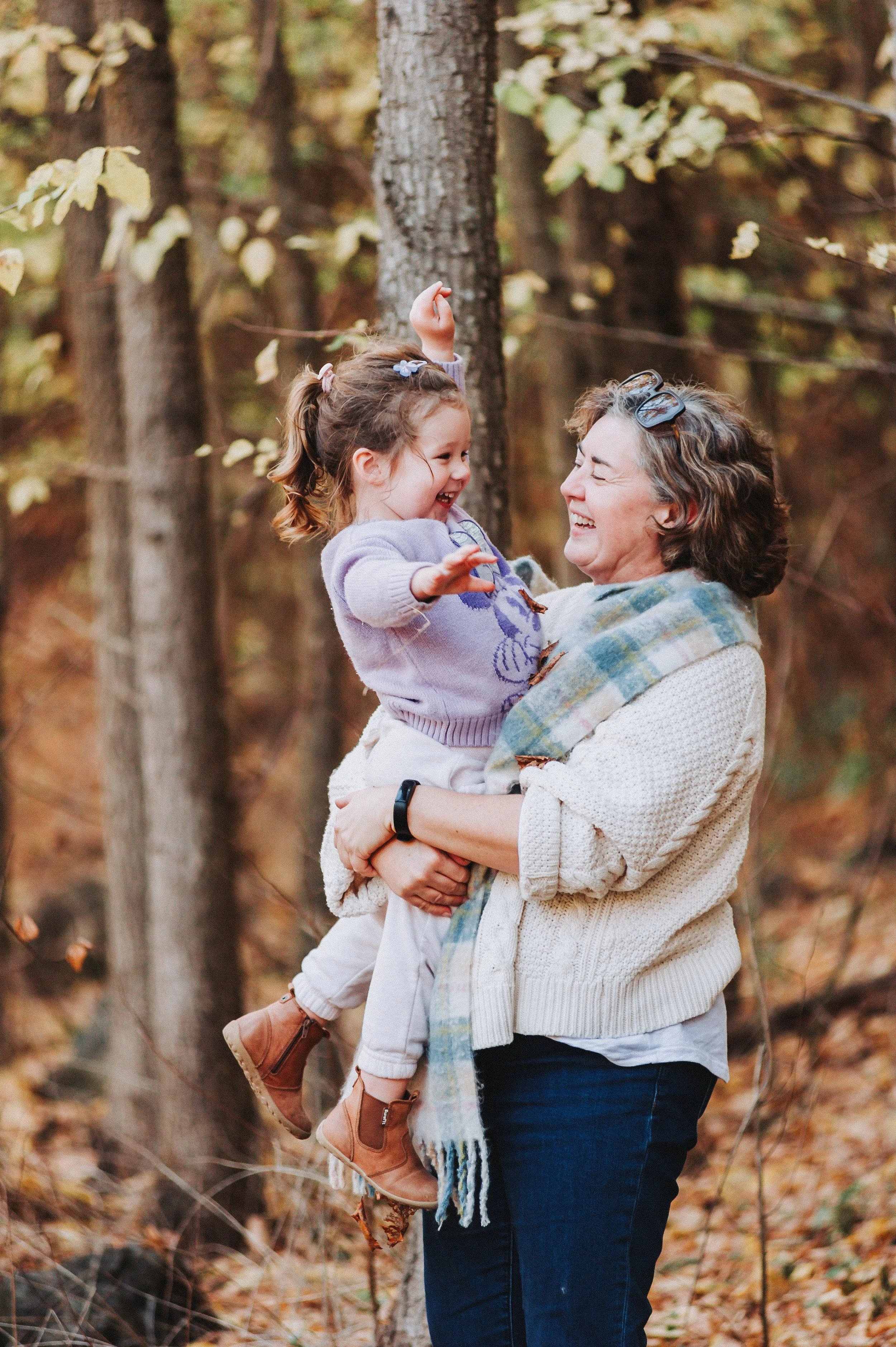 Woman holding a laughing child in a forest setting during fall.