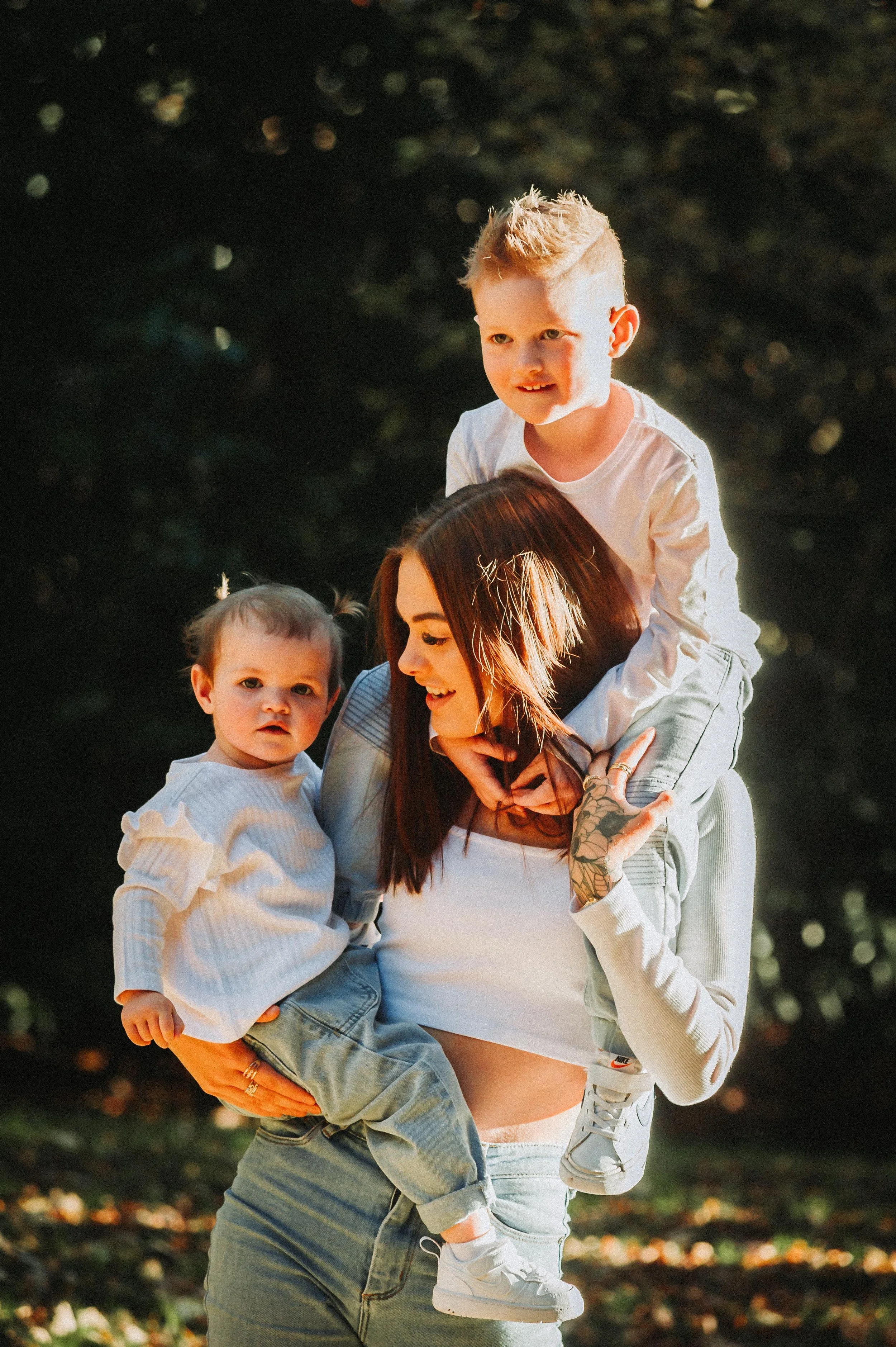 Woman holding two children outdoors with greenery in the background.