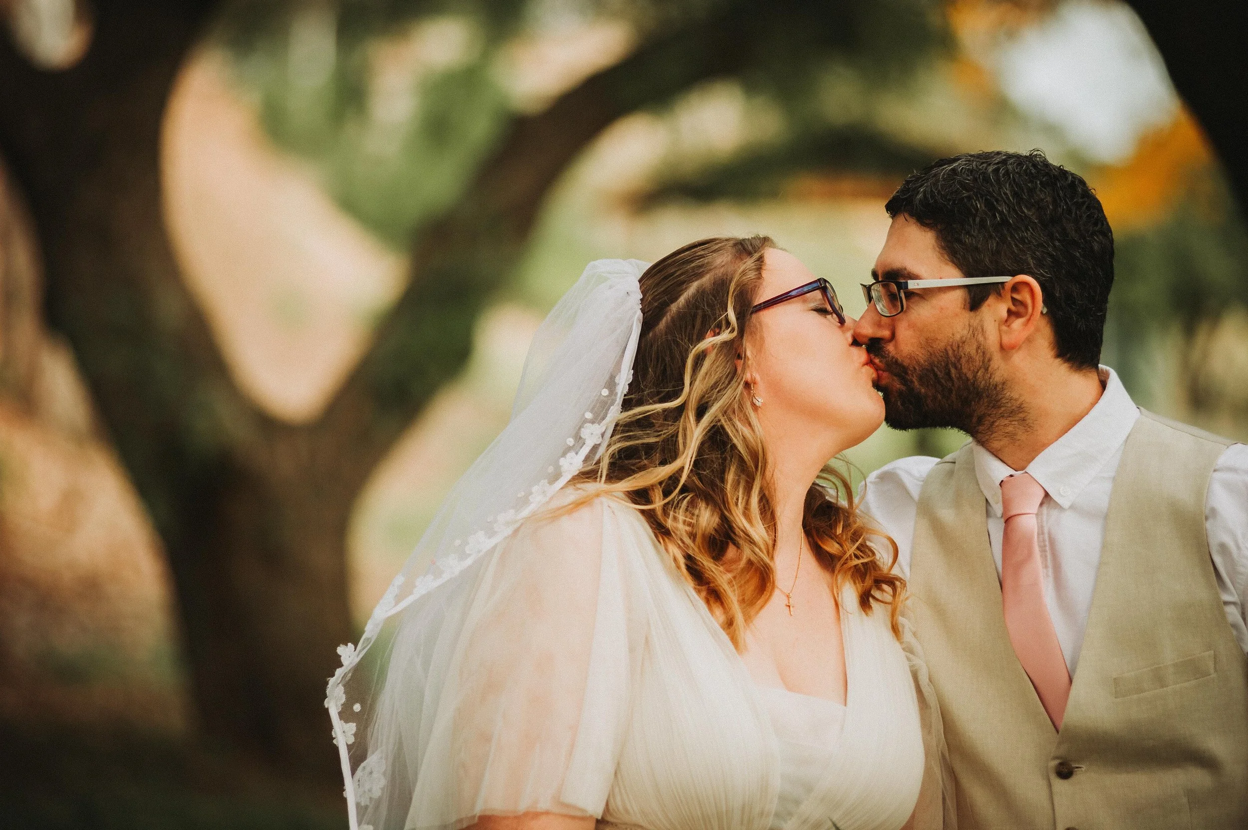 Bride and groom kissing outdoors with trees in the background.