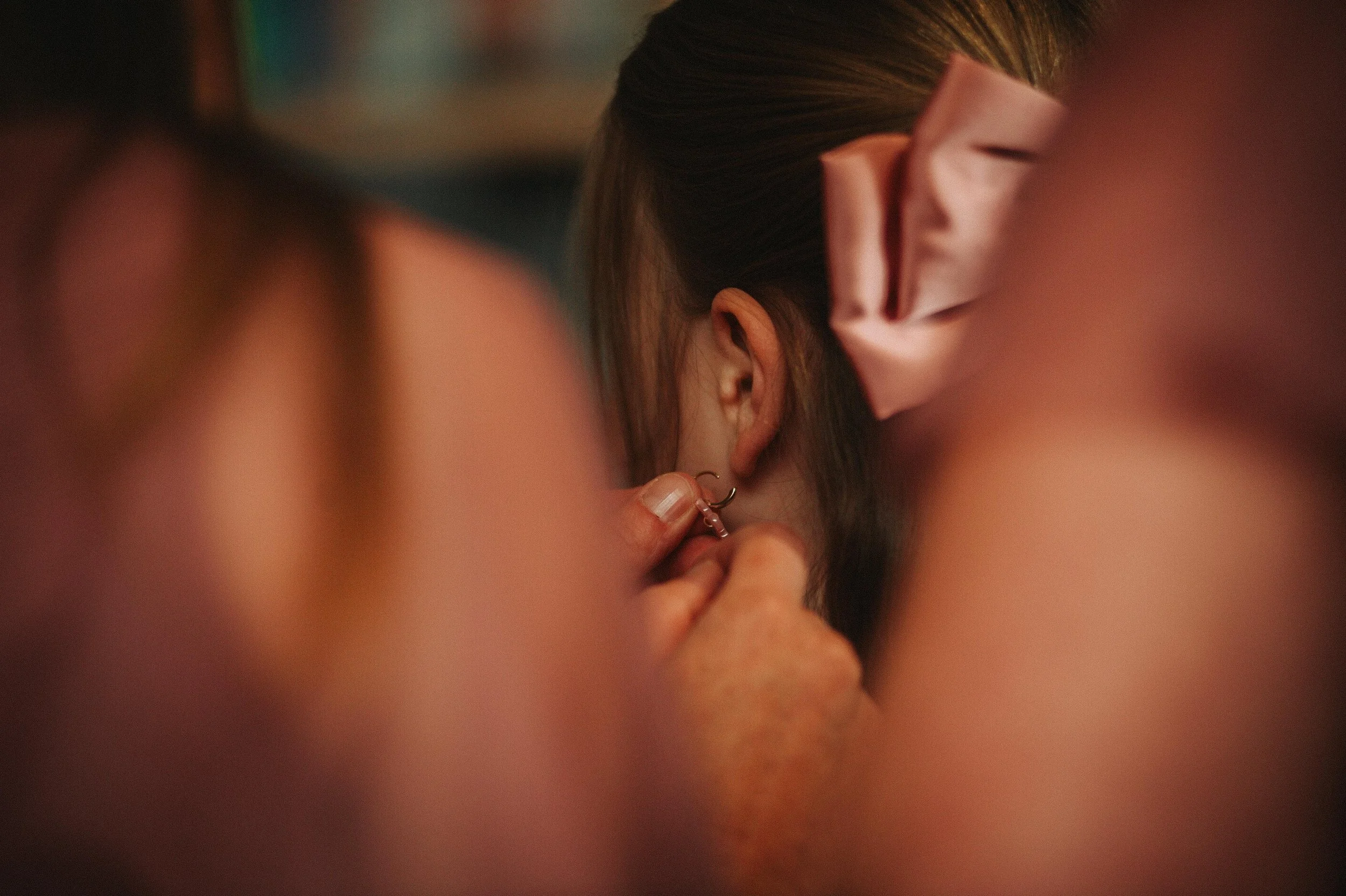 Person putting an earring on a young girl with a pink bow in her hair.