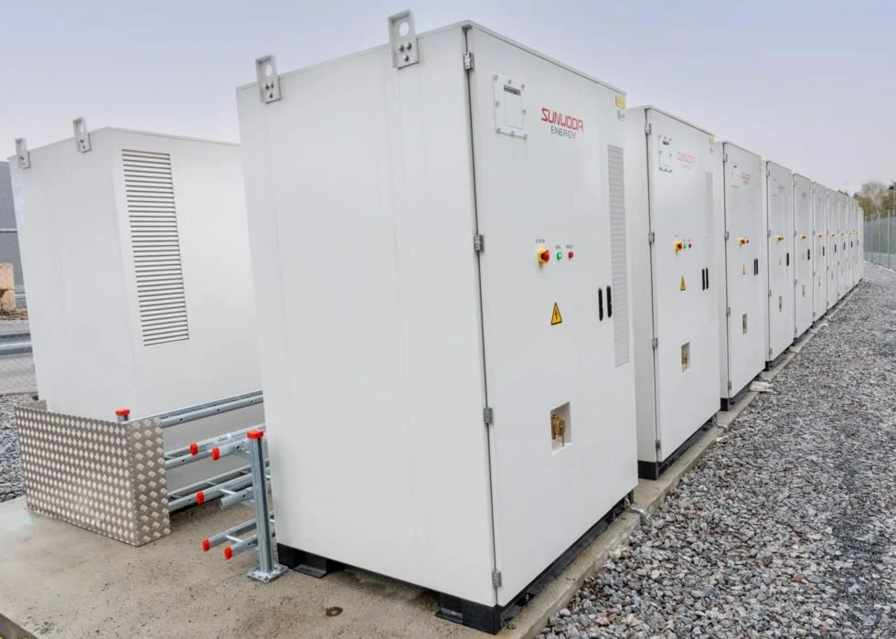 Series of white solar energy inverters installed outdoors on a gravel surface.