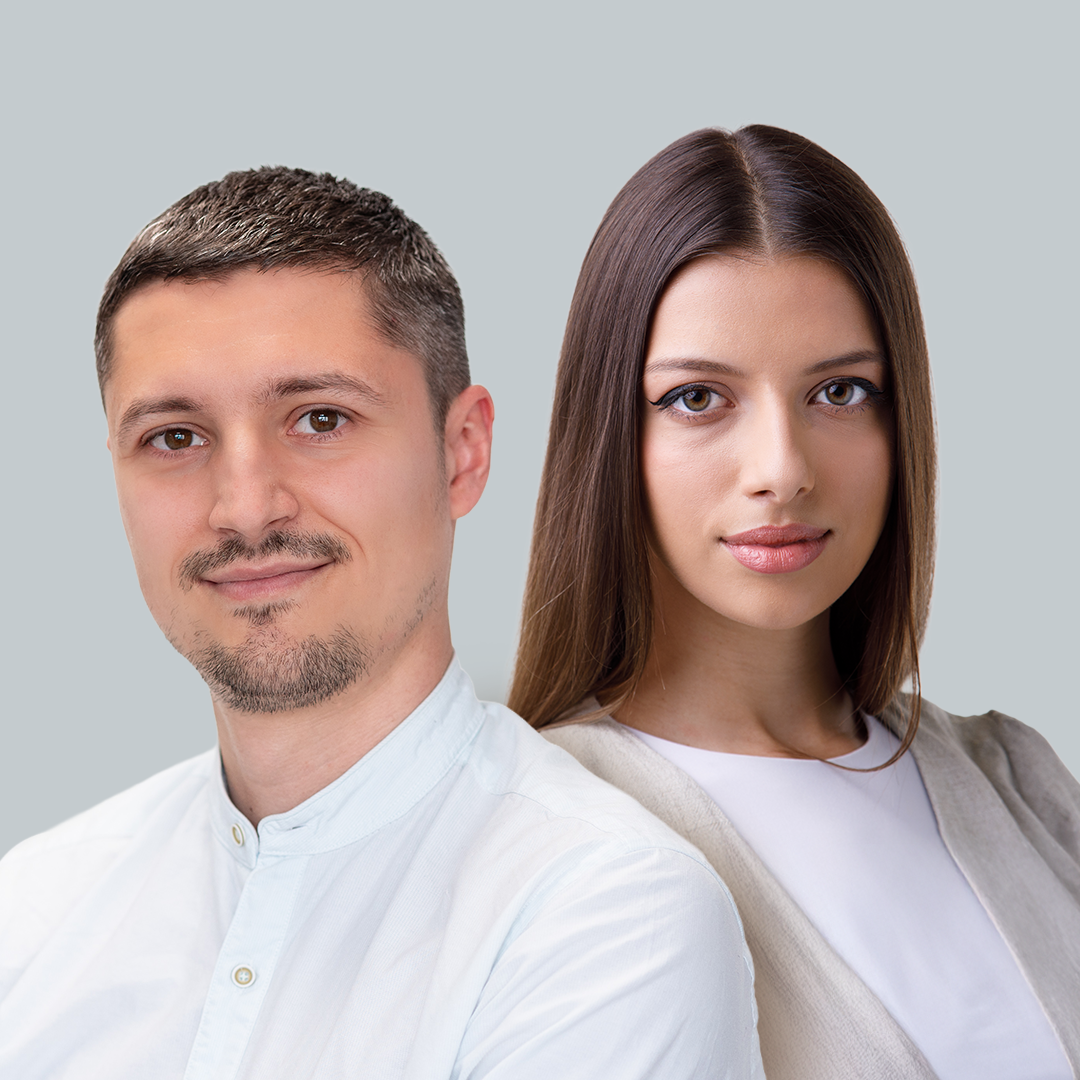 A man with short brown hair, light complexion, and a goatee, and a woman with long brown hair, light complexion, wearing makeup, both looking at the camera against a plain grey background.
