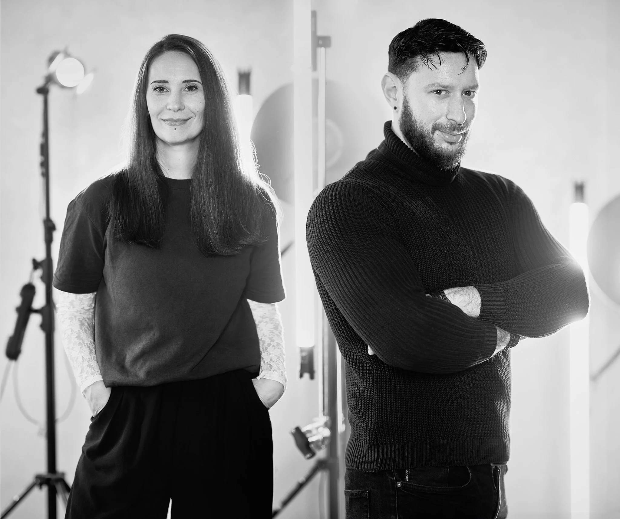 A woman and a man standing in a photography studio with professional lights and equipment visible in the background.