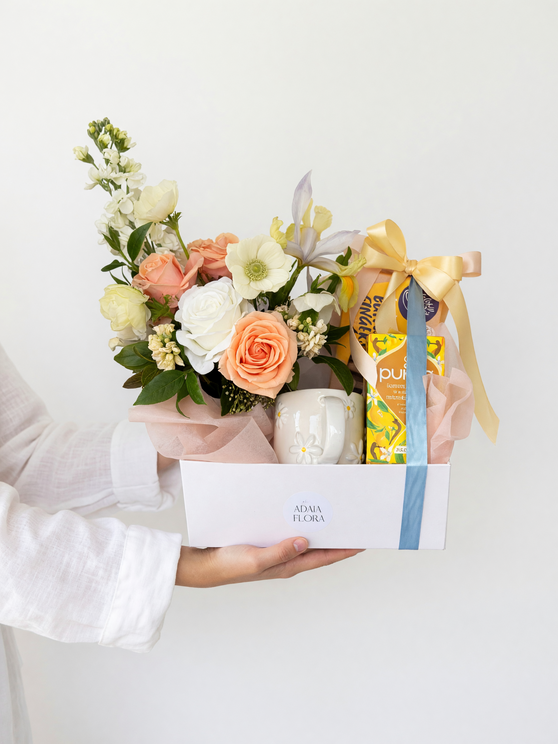 Blue Skies gift hamper beautifully arranged with a potted flower arrangement, daisy mug, lemon and honey tea, chocolate shortbread and gourmet treats by Adaia Flora.