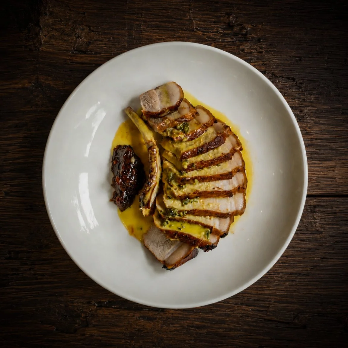 Sliced roasted pork tenderloin with a yellow sauce and a side of fig jam on a white plate, placed on a dark wooden surface.