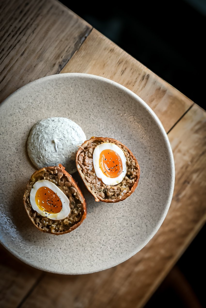 Plate with halved Scotch eggs and a scoop of dip or sauce on a wooden table.