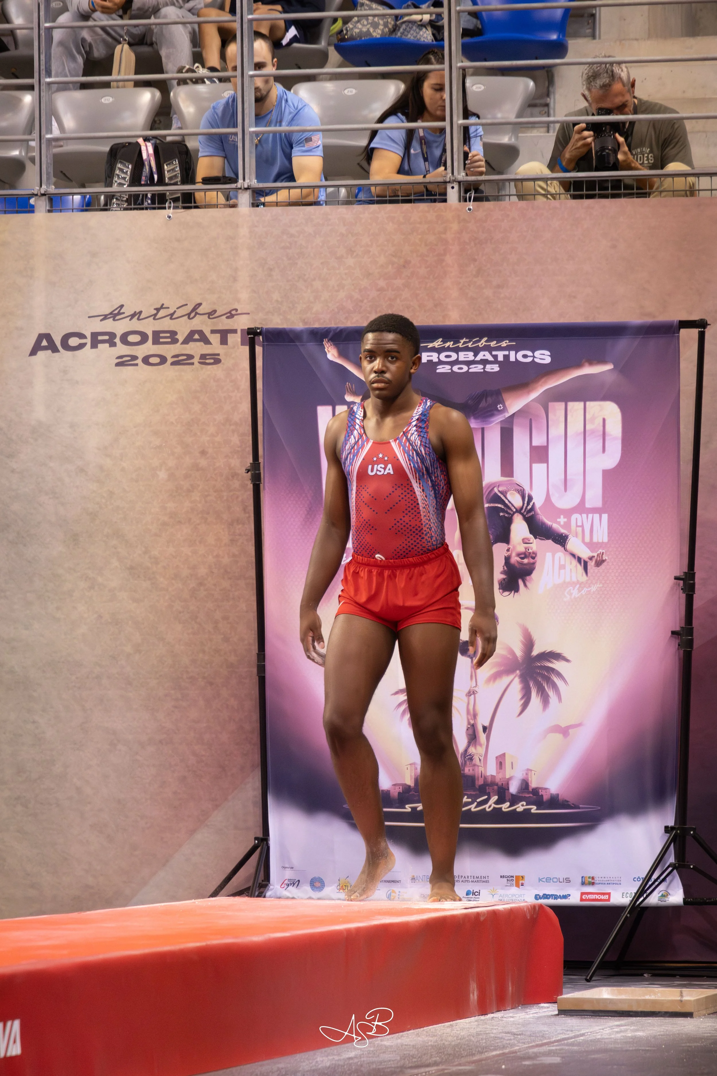 Un athlète en tenue de gymnastique prêt à participer à une compétition, avec un public et des juges en arrière-plan.