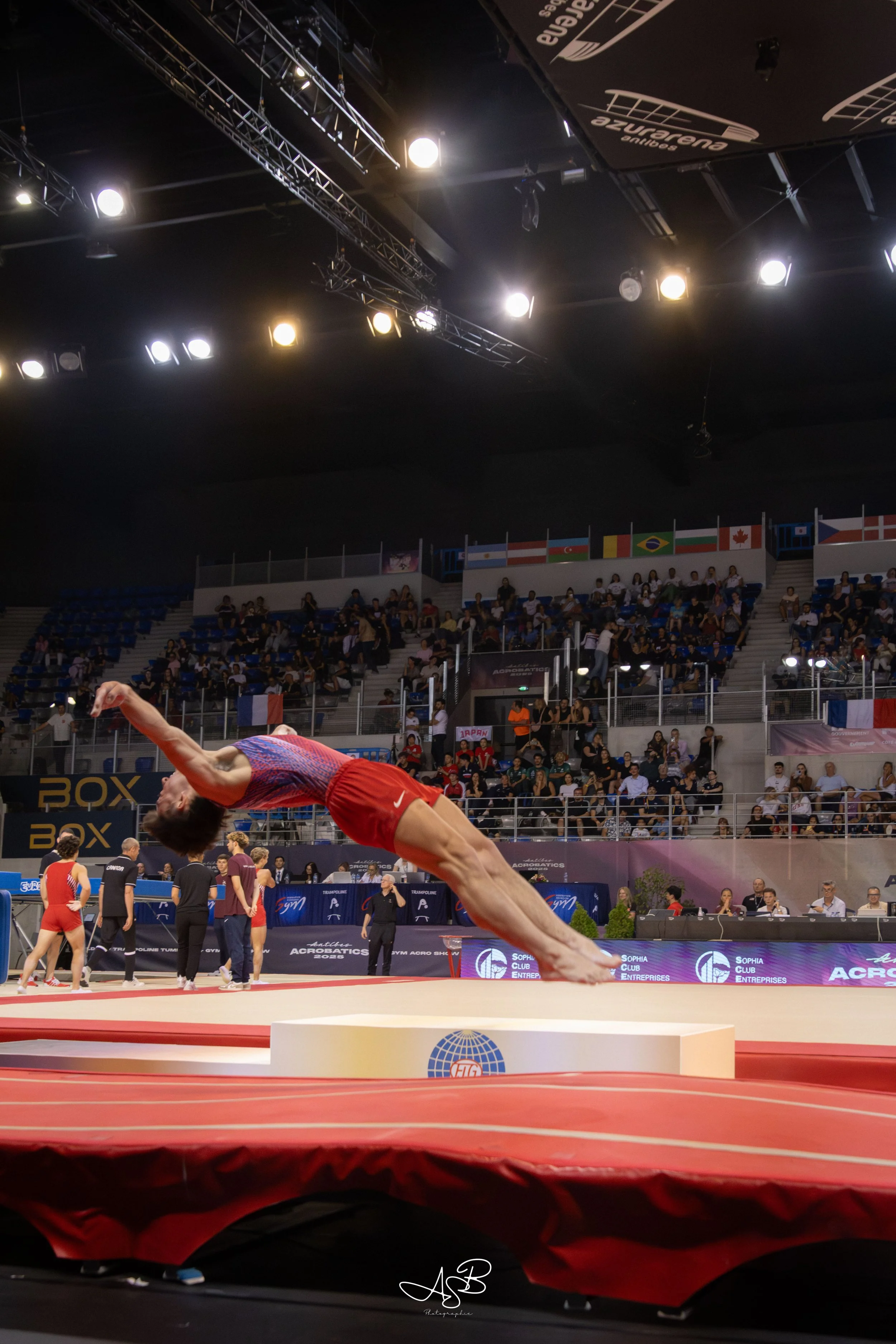 Un gymnaste en plein saut lors d'une compétition sur la table de saut, avec un public dans les gradins en arrière-plan.