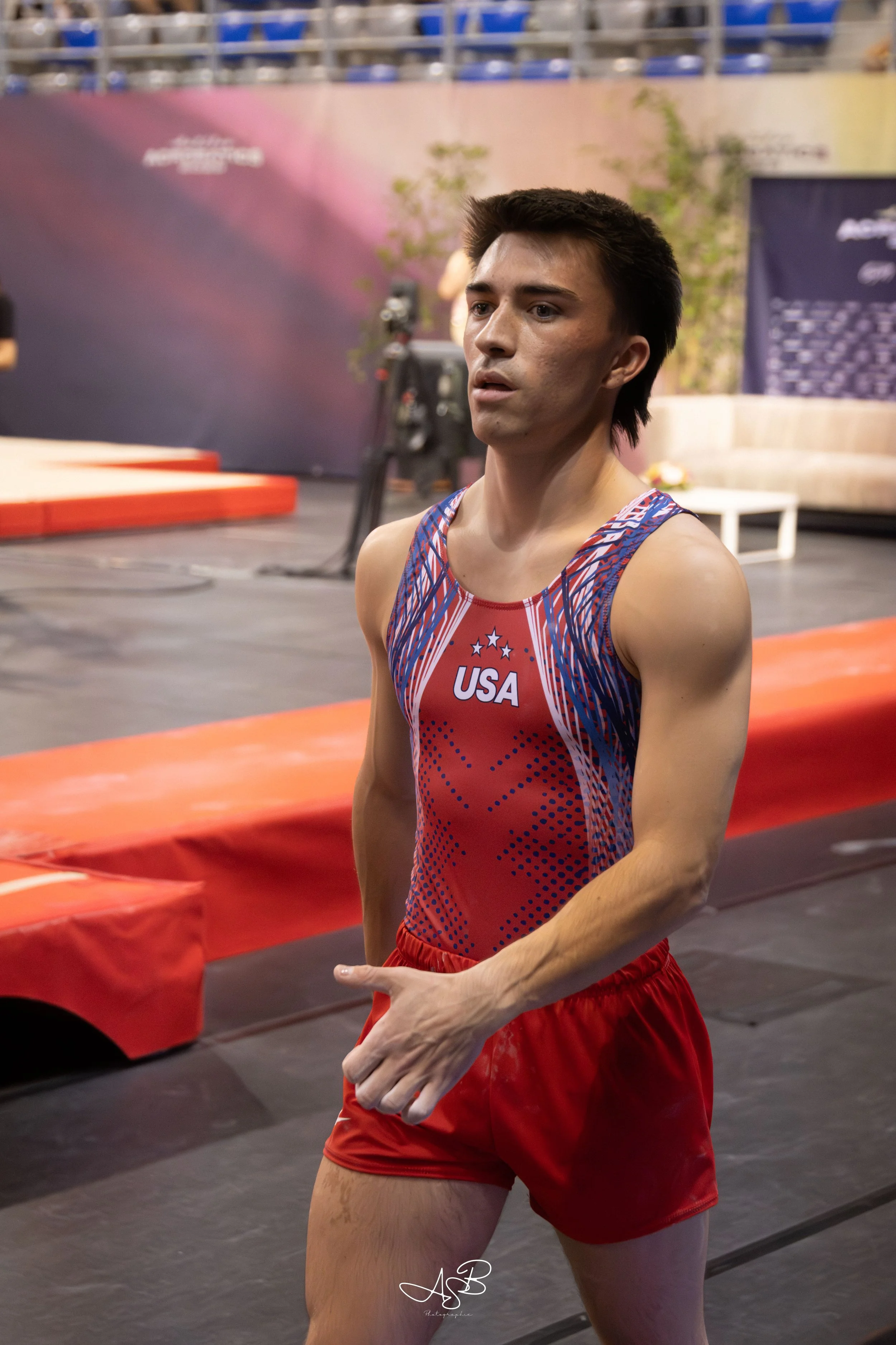 Un athlète américain en tenue rouge et bleu dans une salle d'entraînement ou de compétition.