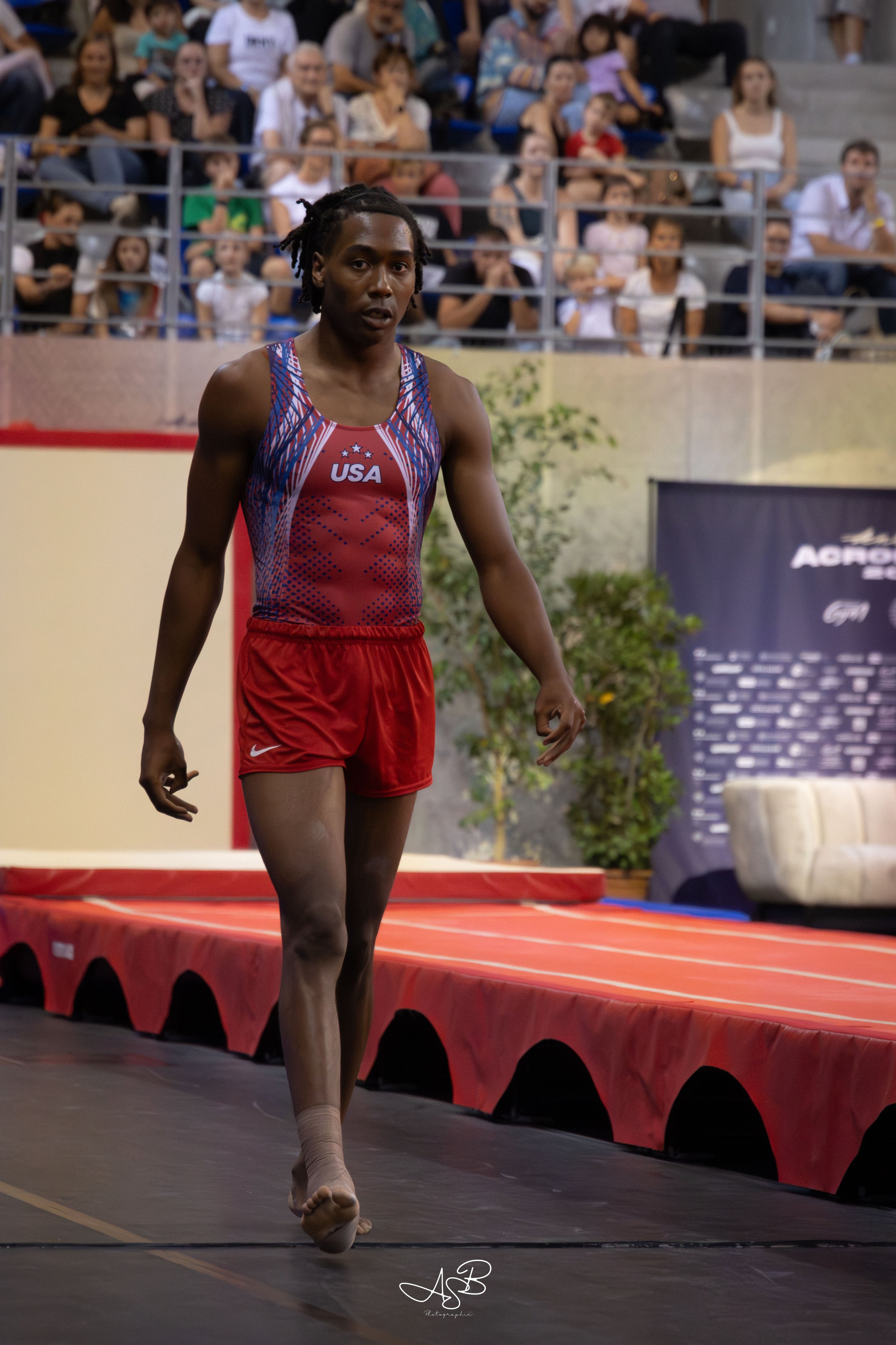 Athlète de l'équipe USA lors d'une compétition de saut en longueur, marchant sur la piste intérieure, avec un public dans les gradins en arrière-plan.