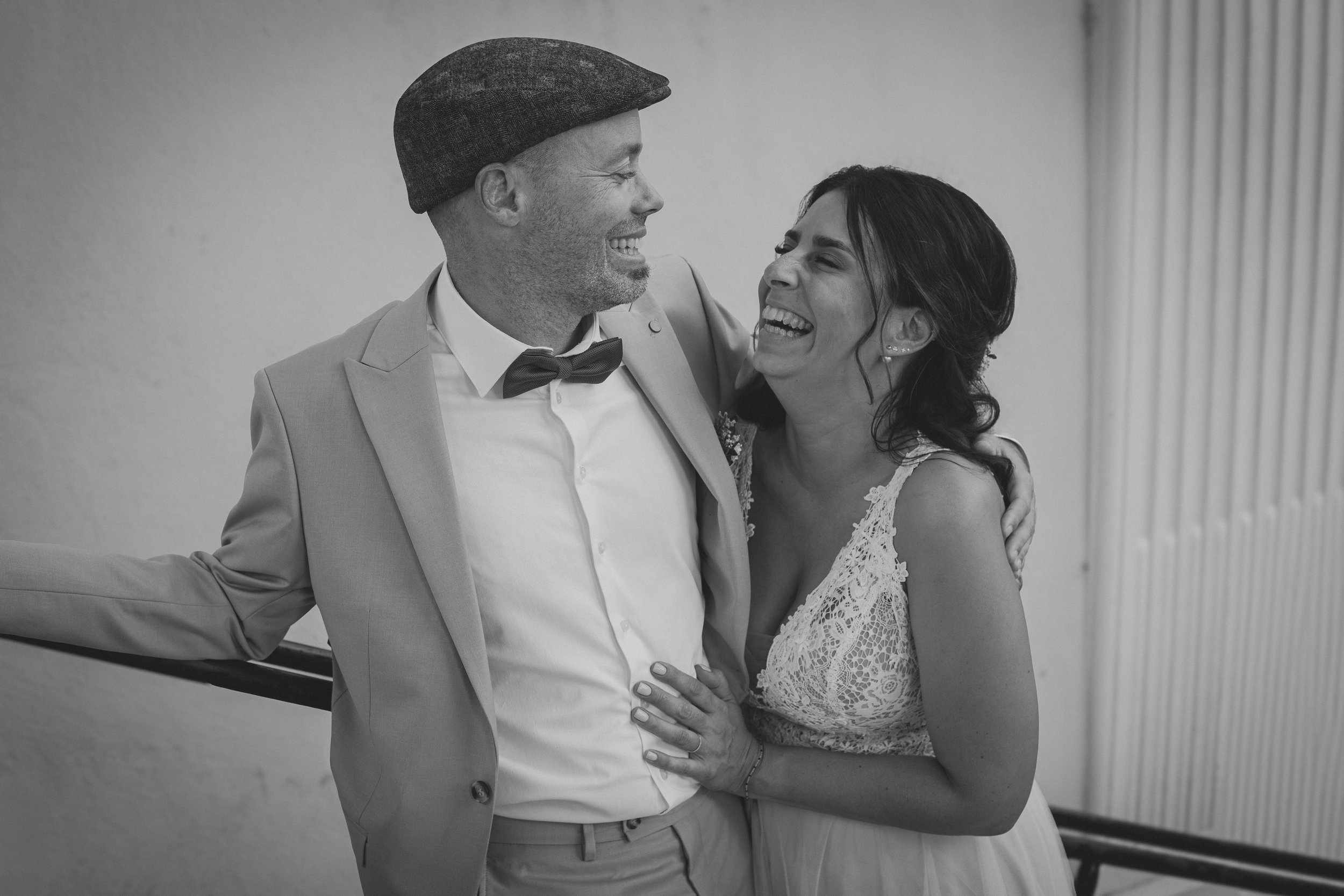 Un homme et une femme souriants, en tenue de mariage, s'embrassant dans une pose affectueuse lors d'une cérémonie. La femme porte une robe en dentelle et l'homme un costume avec un nœud papillon.