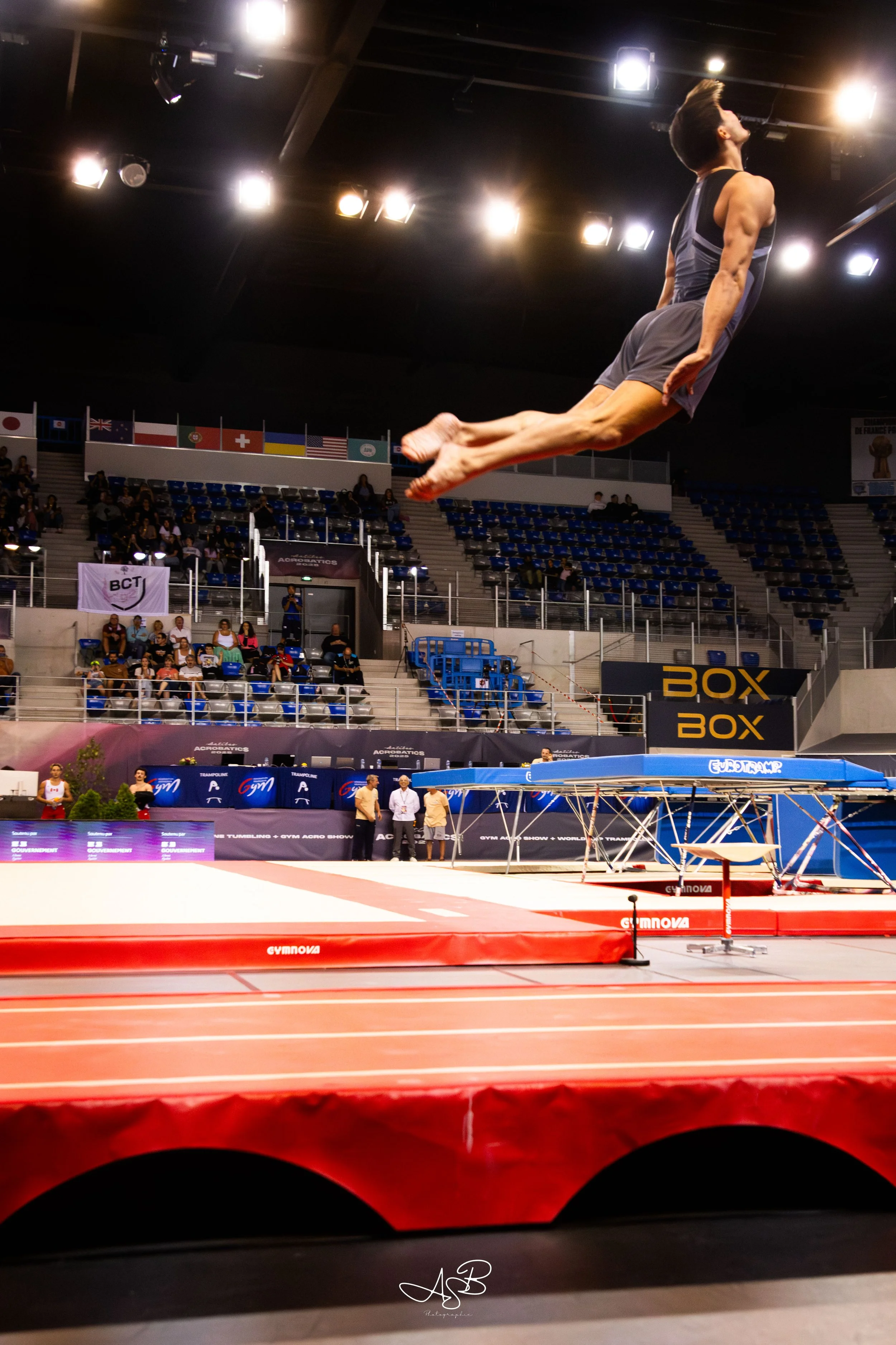 Un homme en plein saut lors d'une compétition de gymnastique dans une arène.