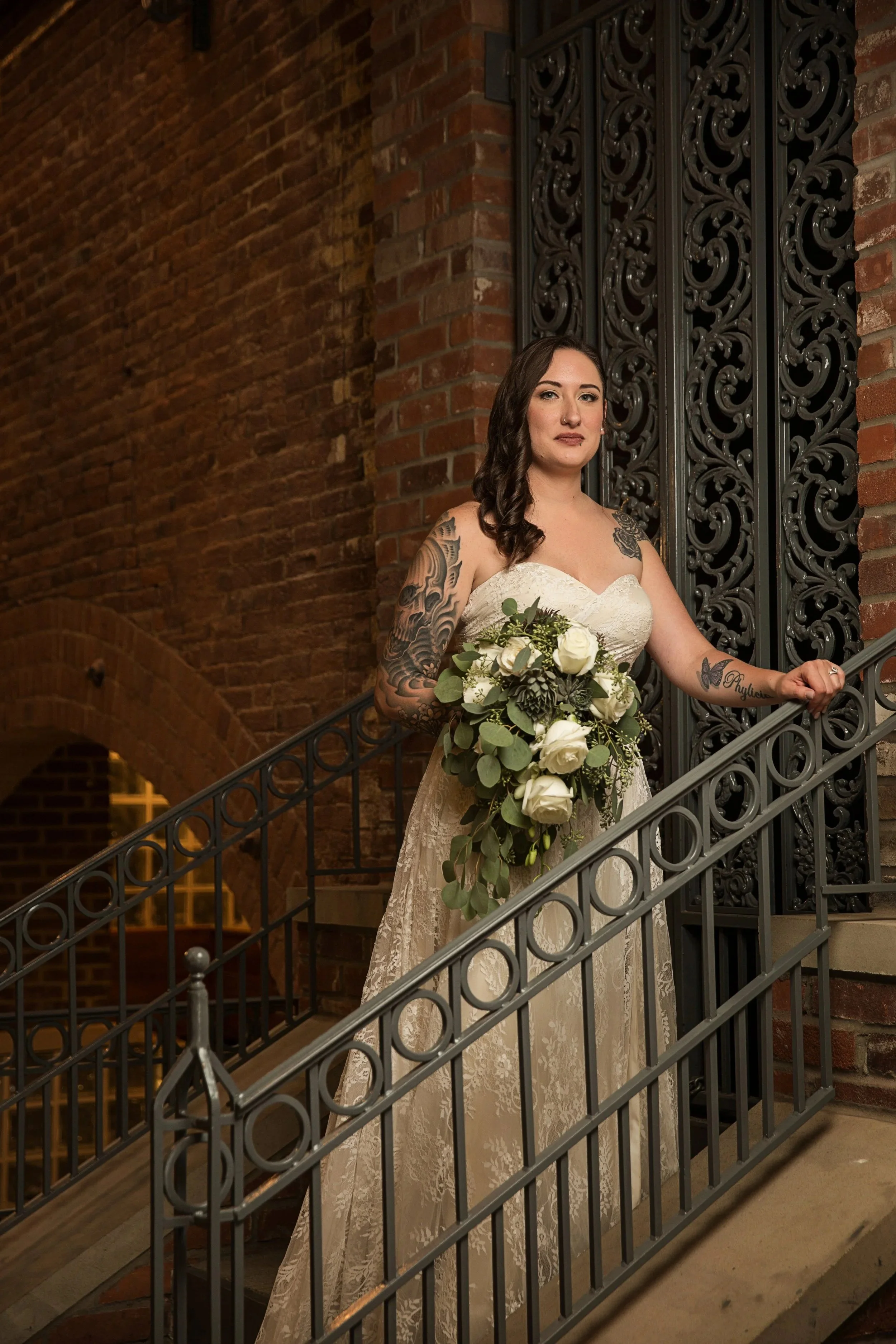 Bride with soft glam makeup and floral bouquet posing on a staircase inside an Indianapolis Indiana wedding venue.