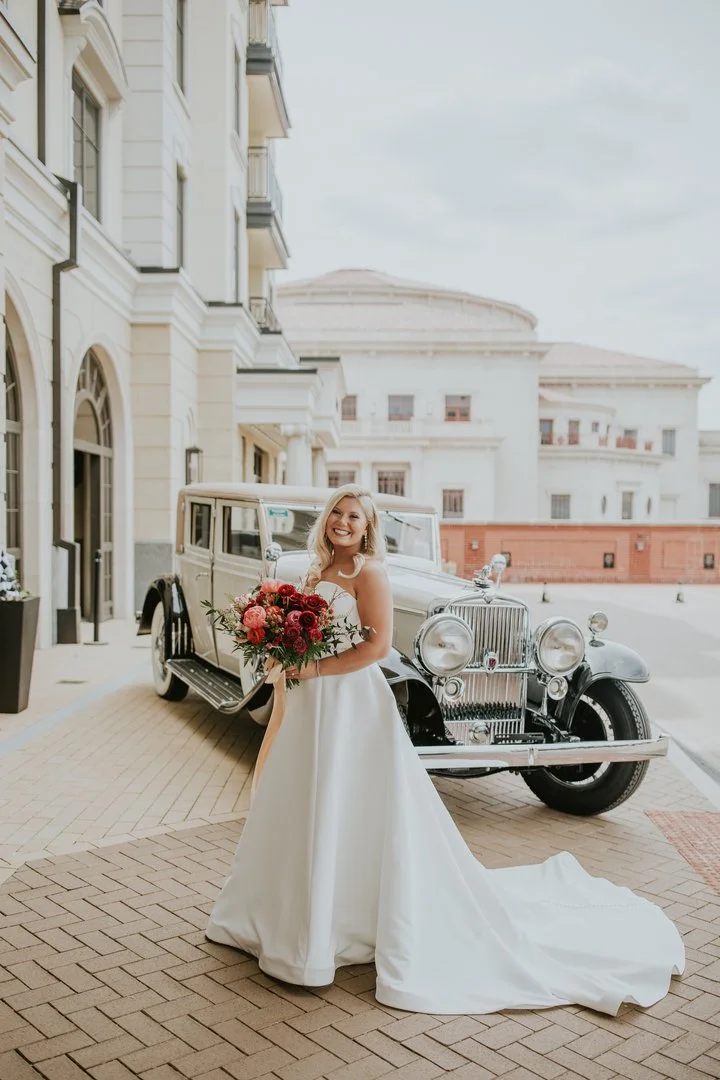 Bride with soft glam bridal makeup standing beside a vintage wedding car outside an Indianapolis venue.