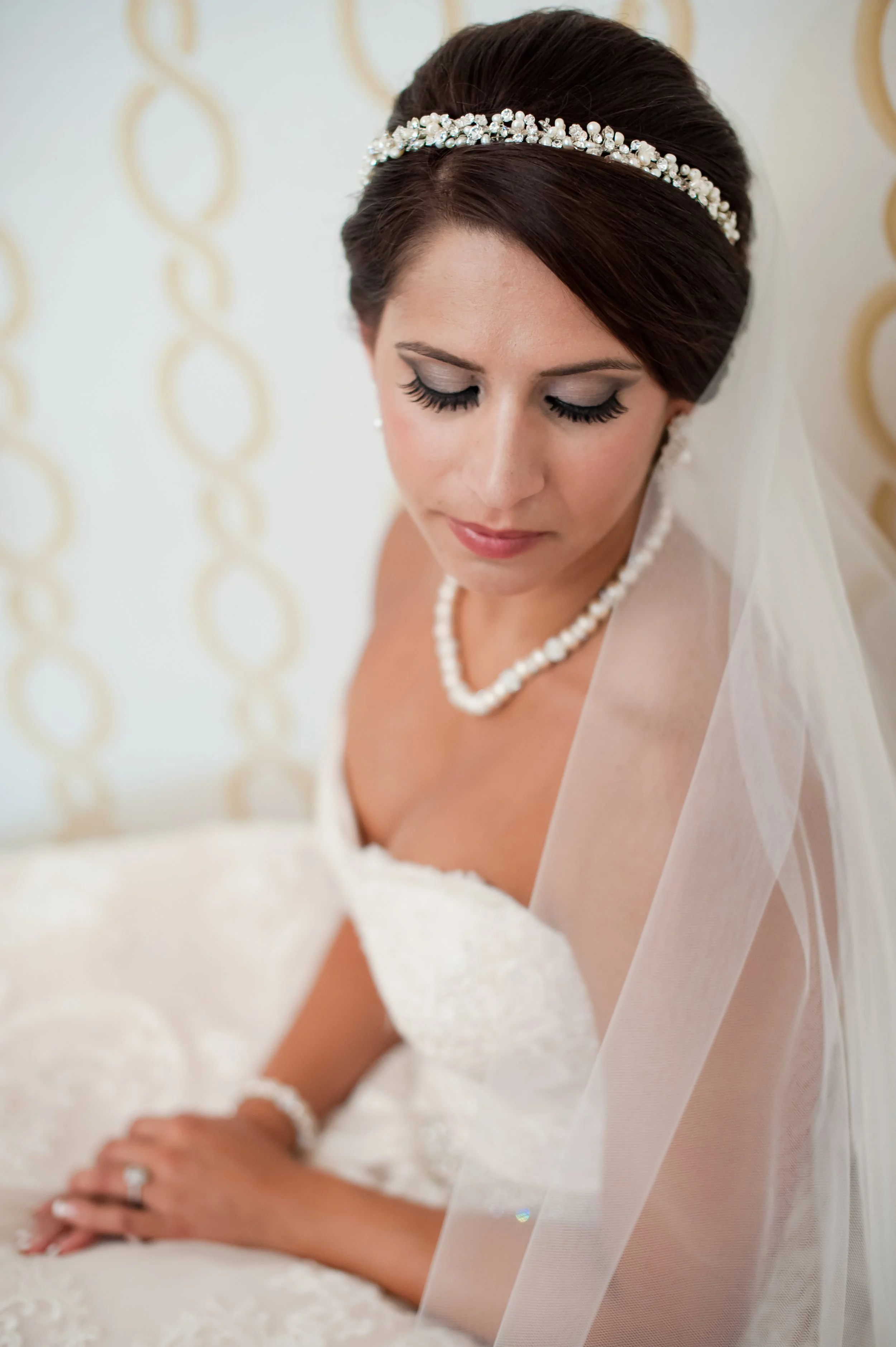An Indianapolis bride in a white wedding dress, pearl necklace, and pearl headband, sitting with her eyes closed and hands clasped, with a sheer veil draped over her shoulder.